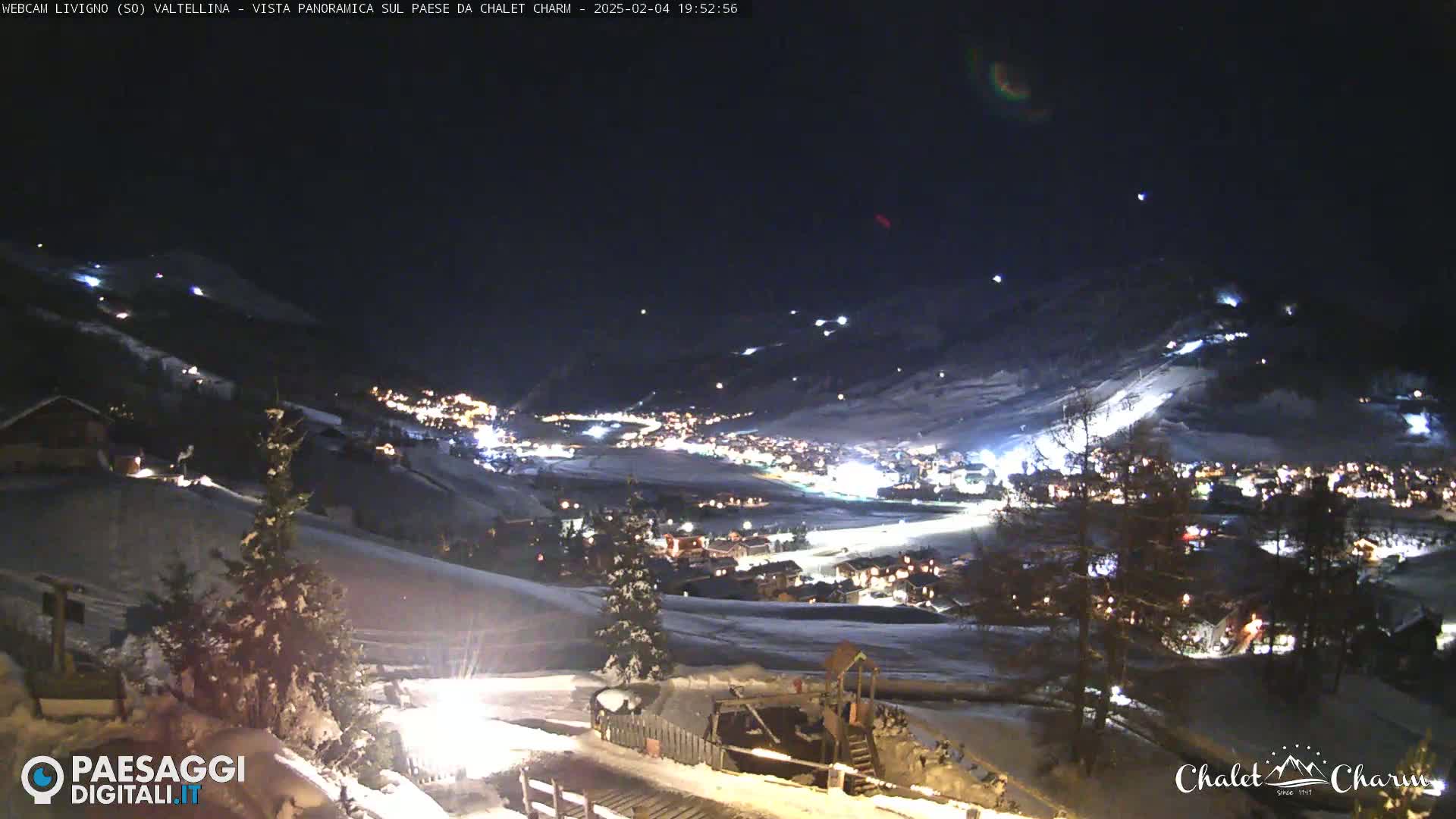 A snow-covered village is illuminated at night, nestled in a valley under a dark sky.