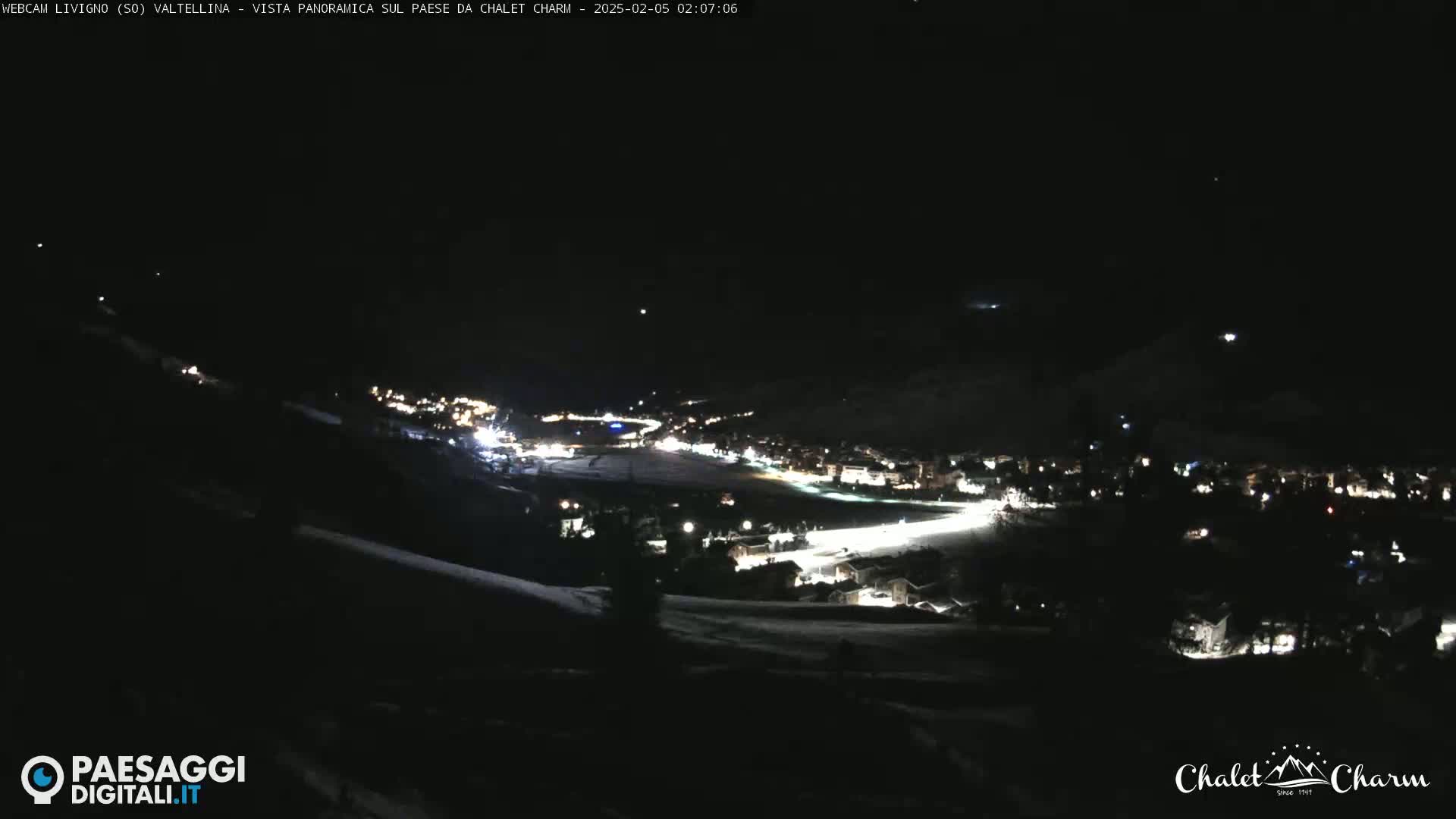 A nighttime panoramic view of a snow-covered village illuminated by lights, under a clear, dark sky.