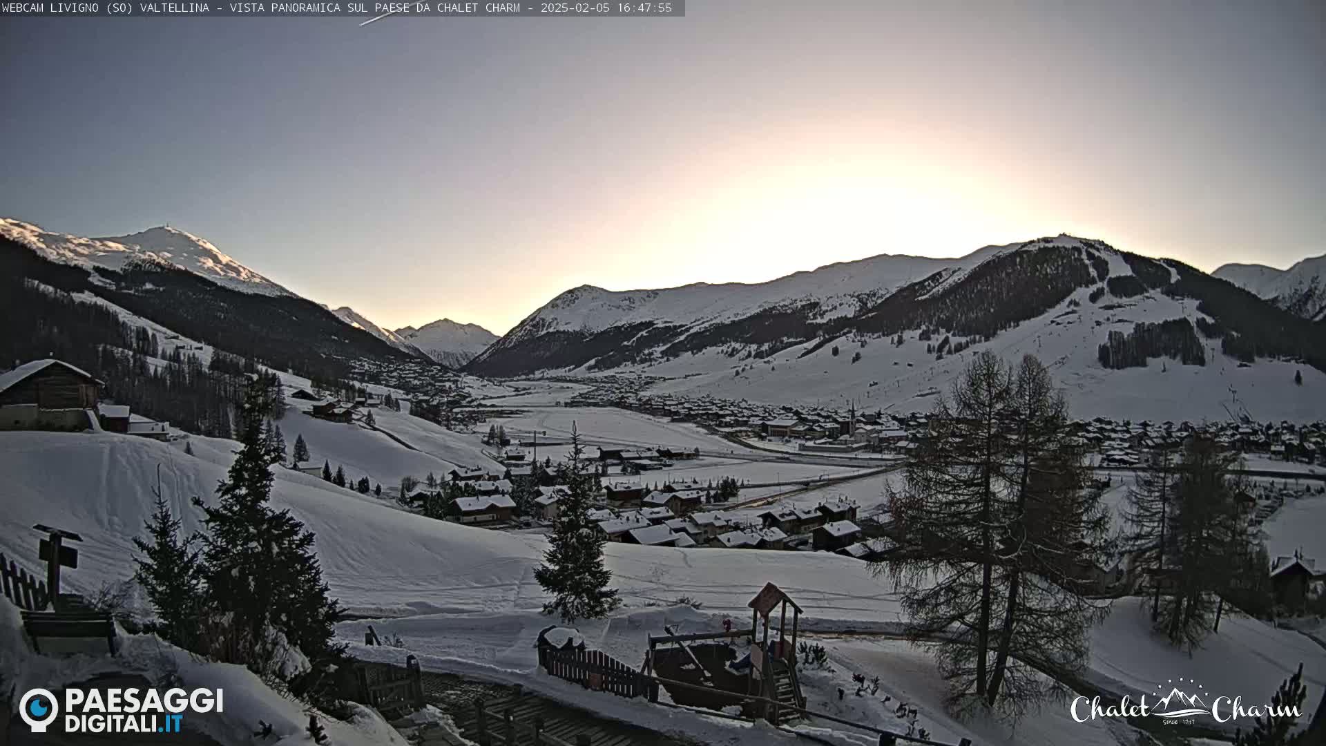 A snow-covered mountain village is visible at sunset, with snow-covered hills and mountains in the background.