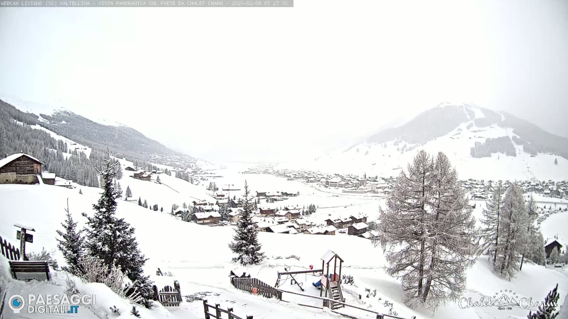A snow-covered village nestled in a valley between snow-dusted mountains under a heavily overcast sky.