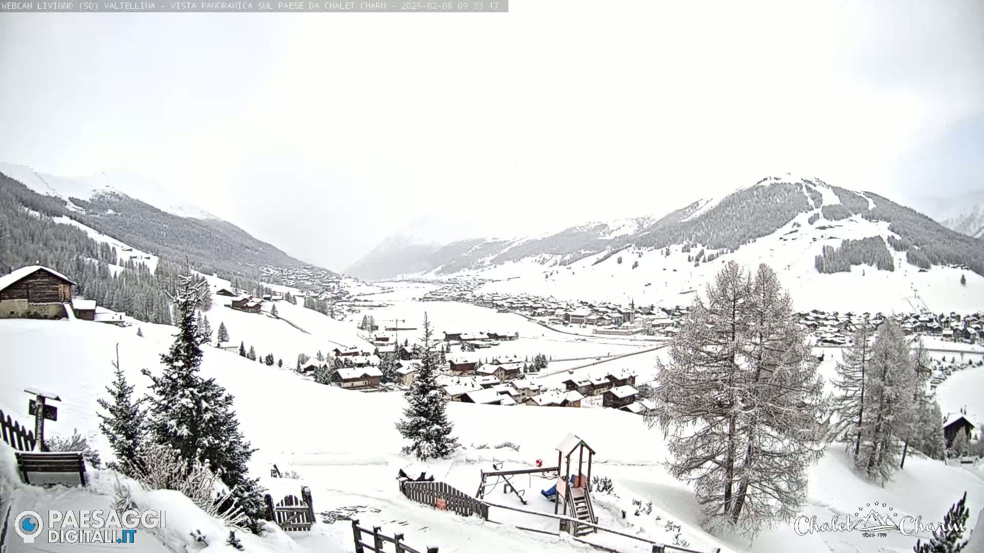 A snow-covered village nestled in a valley between snow-capped mountains under an overcast sky.