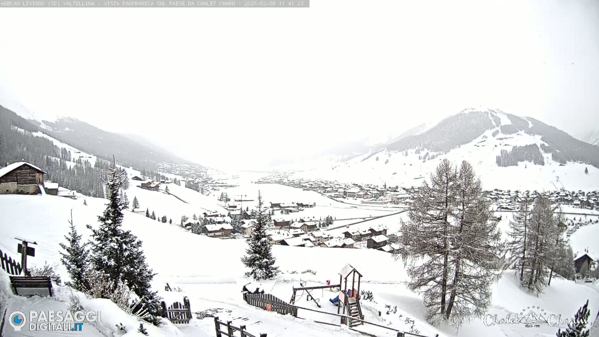 A snow-covered village nestled in a valley between snow-capped mountains under a cloudy sky.
