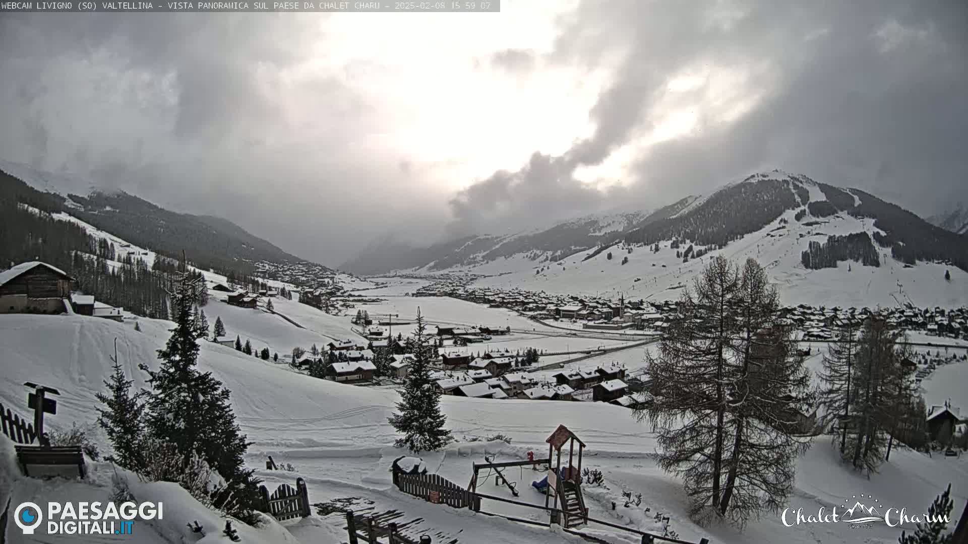 A snow-covered village nestled in a valley between snow-capped mountains under a cloudy sky.