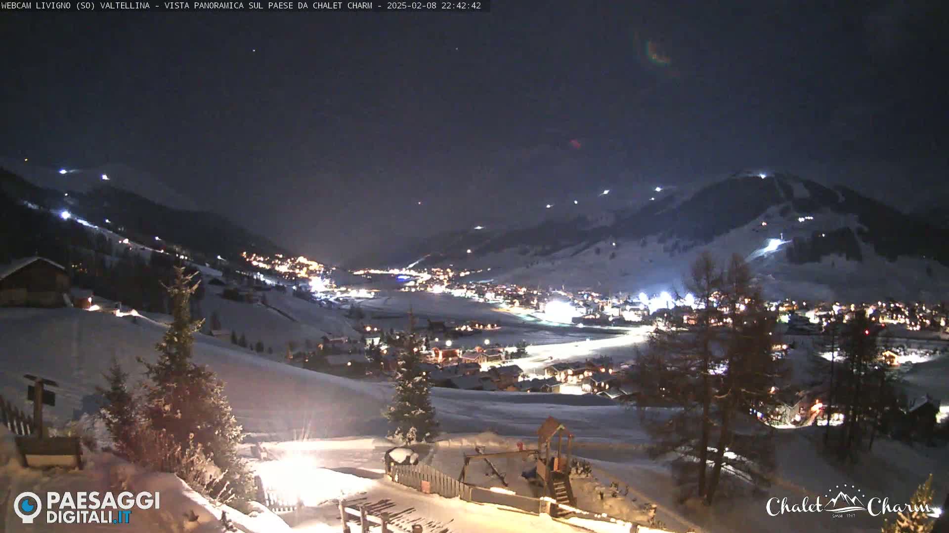 A snow-covered village at night, illuminated by lights, is nestled in a valley under a dark, clear sky.