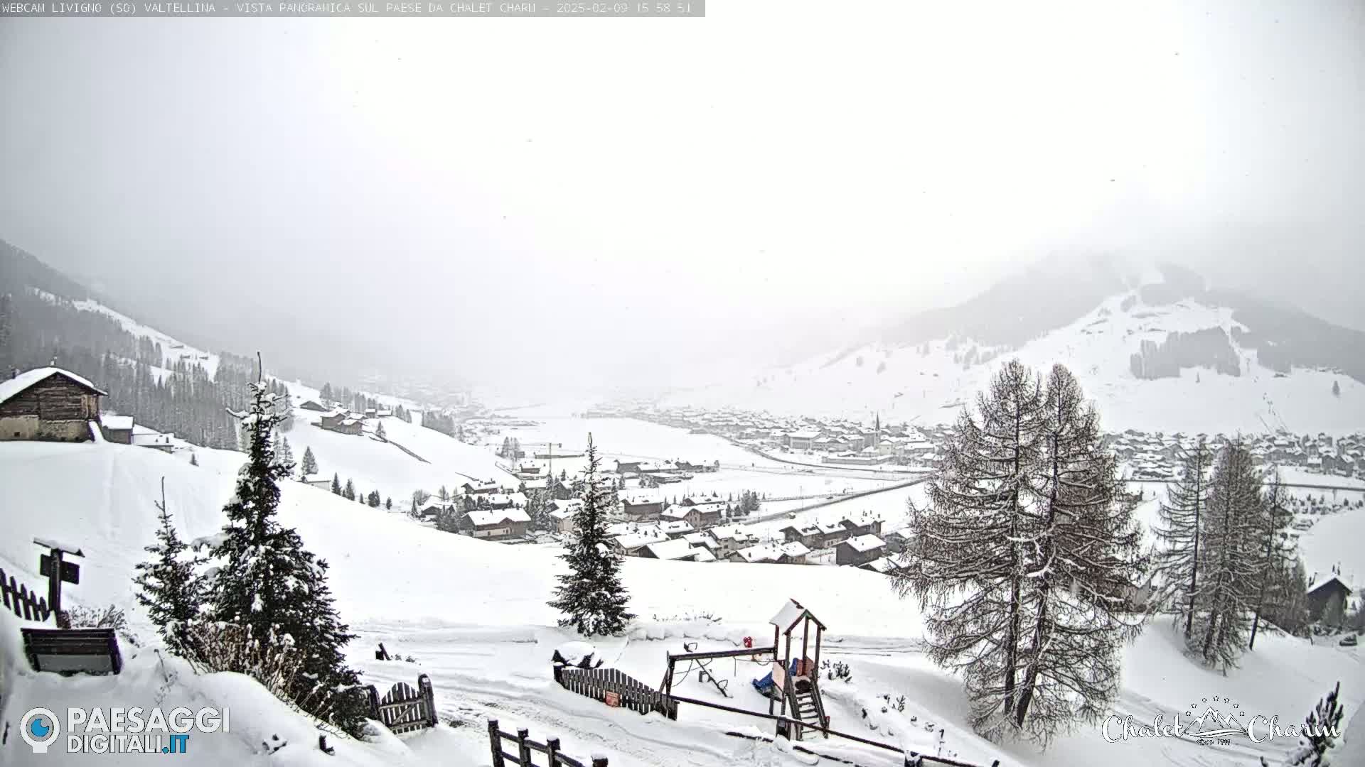 A snowy, overcast vista of a village nestled in a valley between snow-covered hills and mountains.