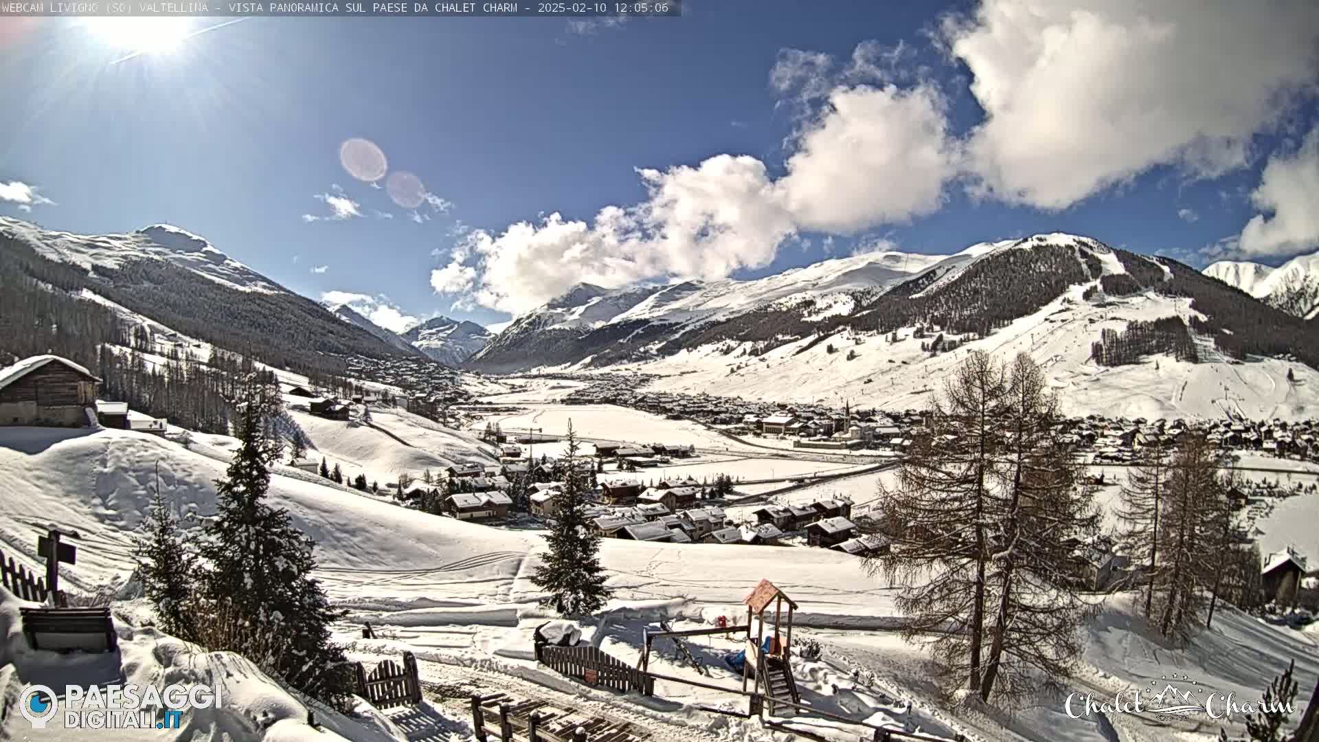 A snow-covered village nestled in a valley between snow-capped mountains under a partly cloudy blue sky.