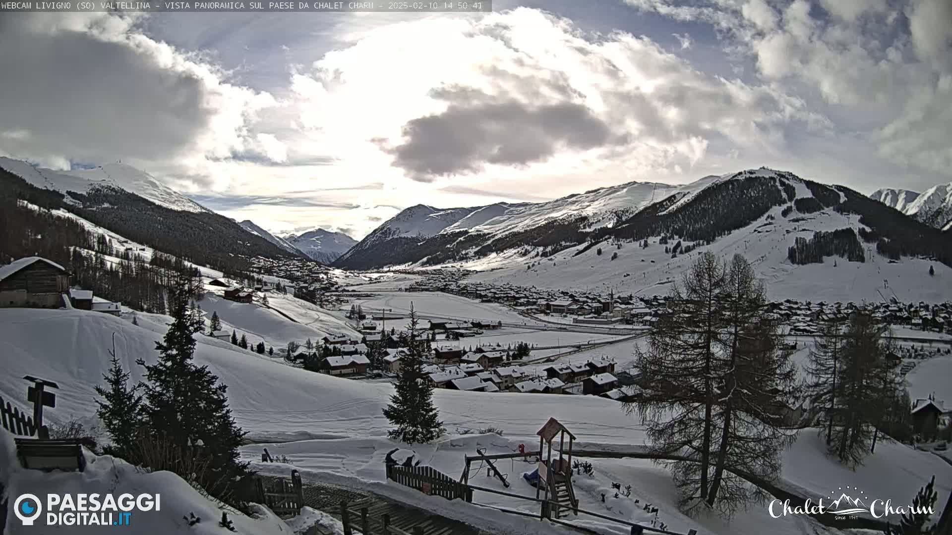 A snow-covered mountain village nestled in a valley under a partly cloudy sky.