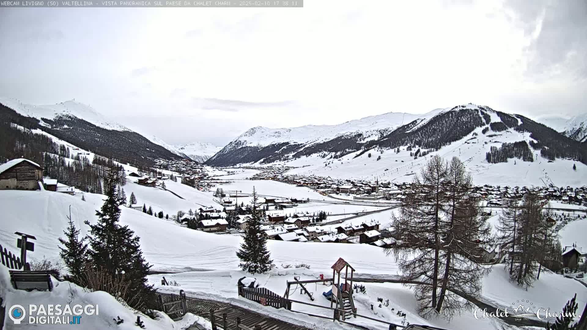 A snow-covered village nestled in a valley between snow-capped mountains under an overcast sky.