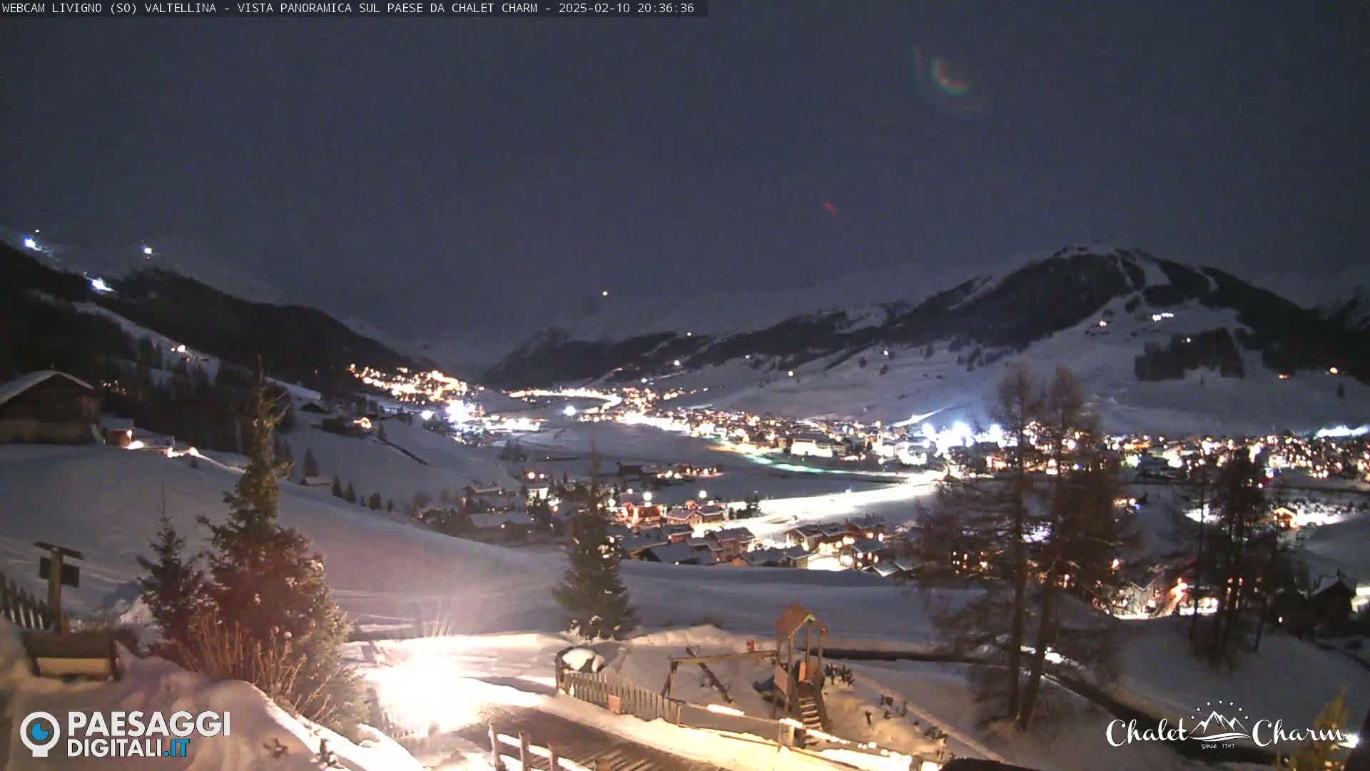 A snow-covered village nestled in a valley at night, illuminated by lights, under a dark, clear sky.