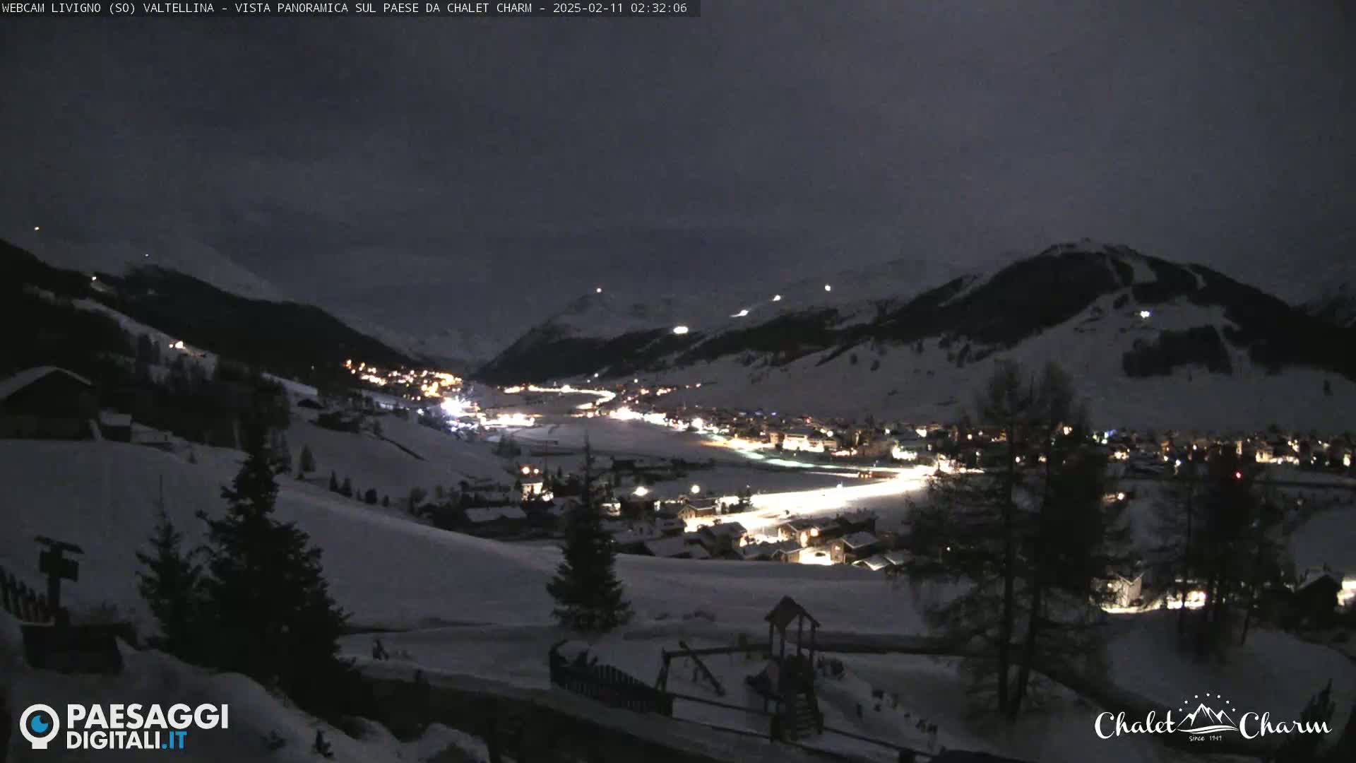 A snow-covered mountain village is illuminated at night, with faint light in the sky.