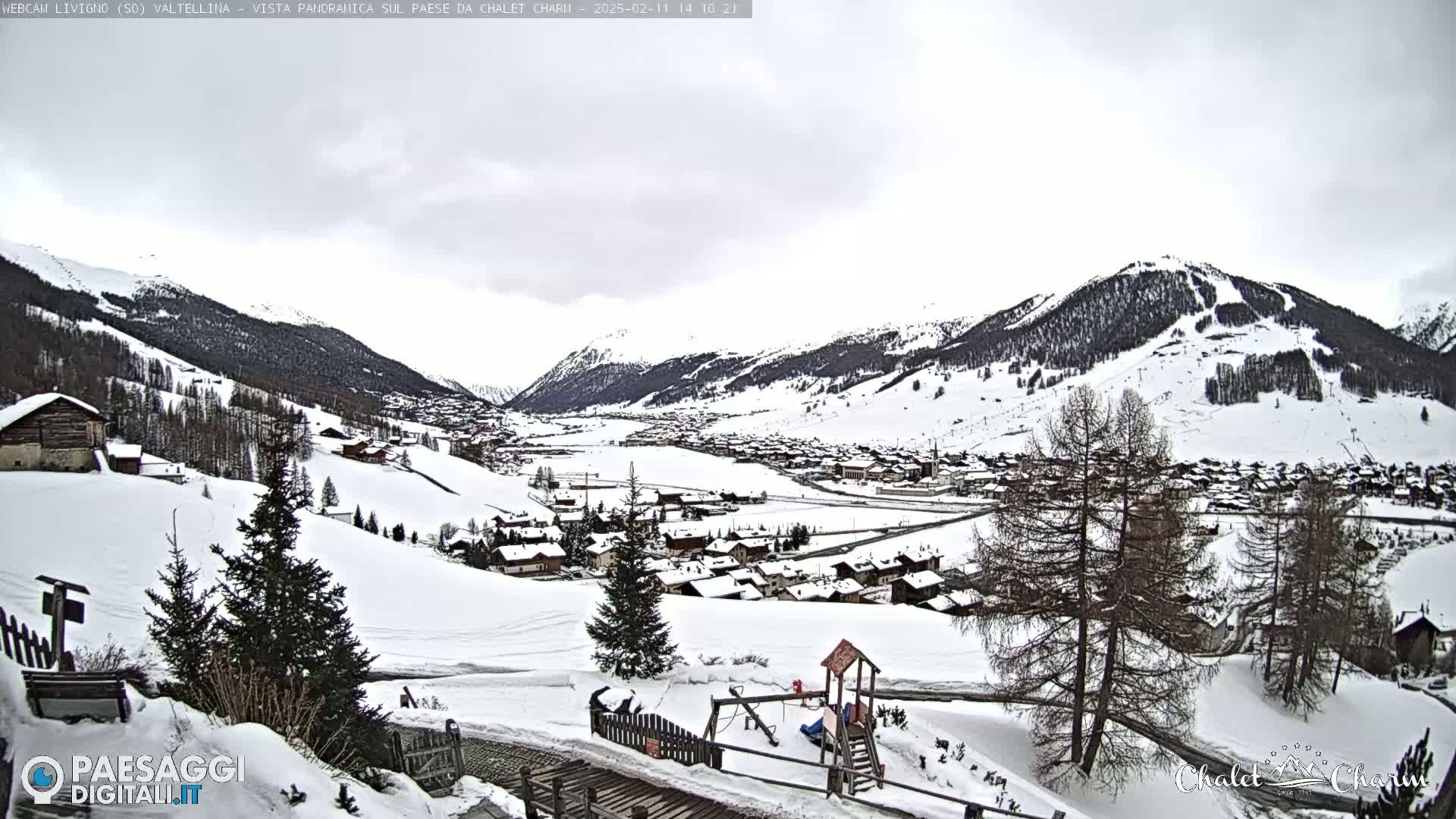 A snow-covered village nestled in a valley between snow-capped mountains under an overcast sky.