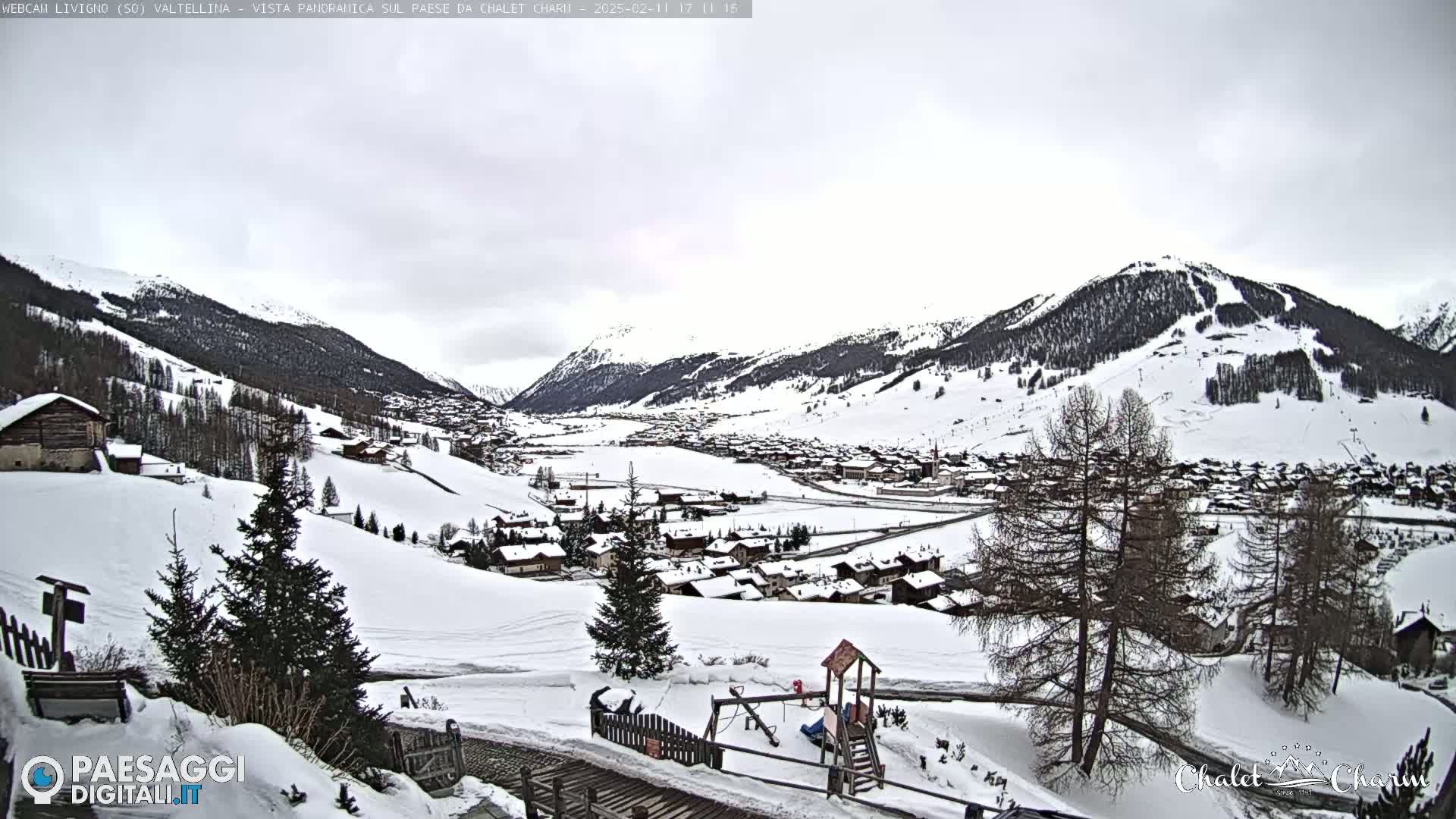A snow-covered village nestled in a valley between snow-capped mountains under an overcast sky.