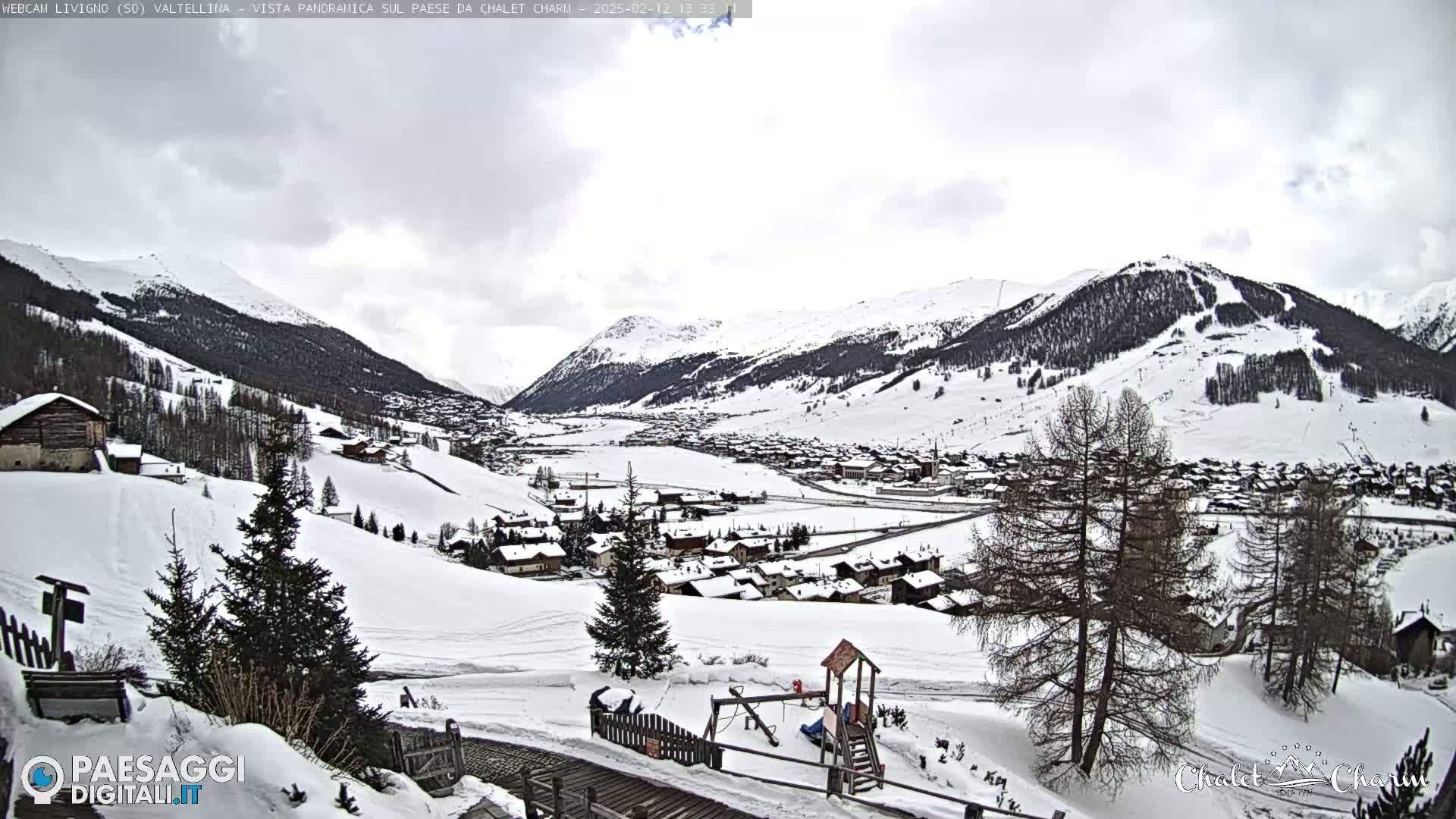 A snow-covered village nestled in a valley between snow-capped mountains under a cloudy sky.