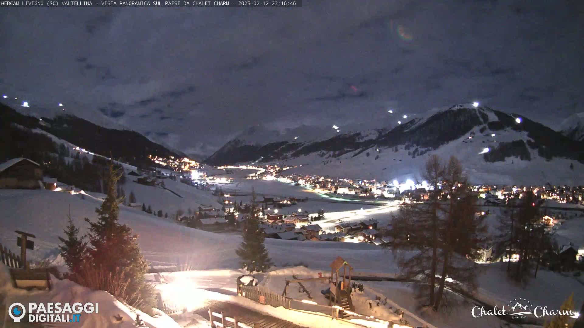 A snow-covered mountain village is illuminated at night under a cloudy sky.