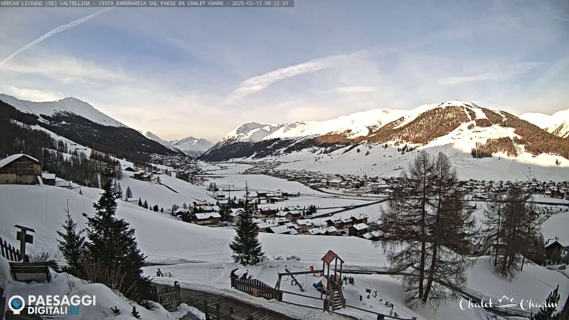 A snow-covered mountain village nestled in a valley, with clear skies and sunlight illuminating the snow-capped mountains in the background.
