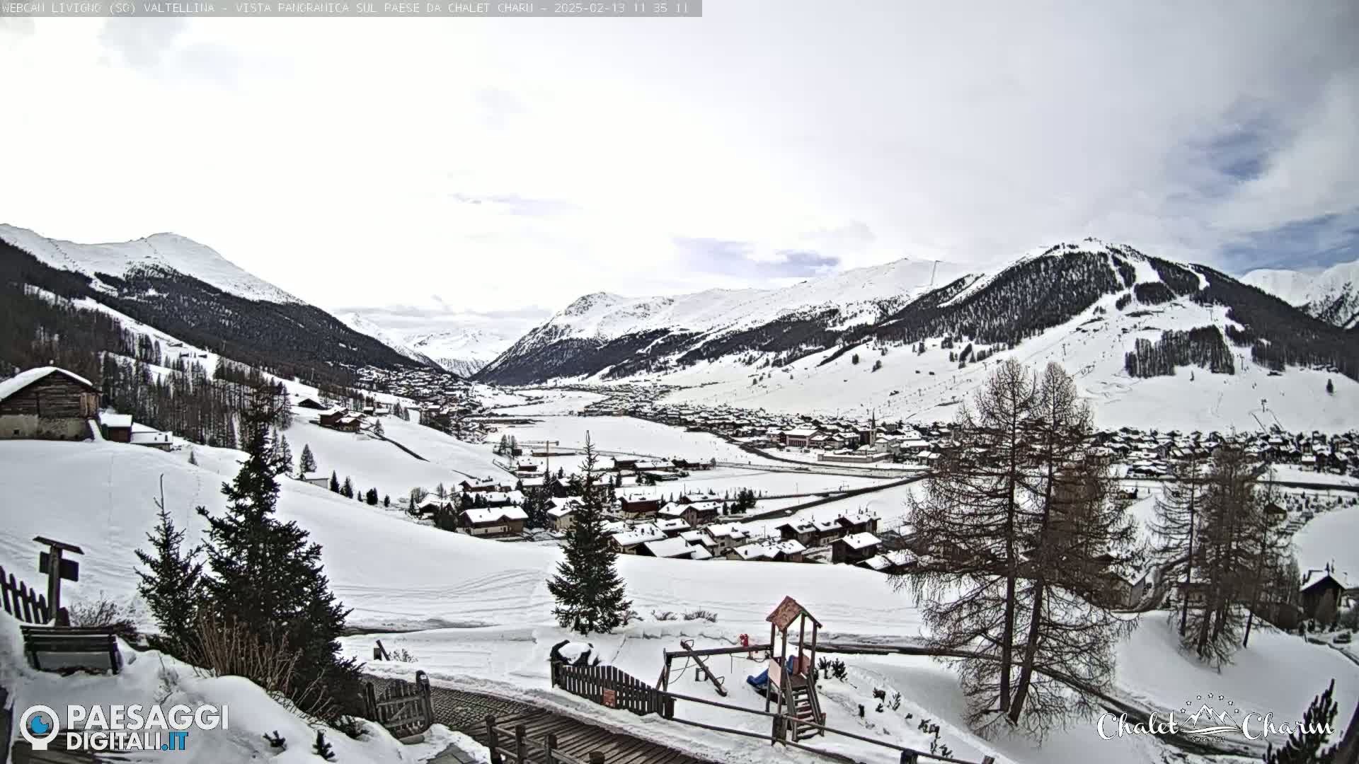 A snow-covered village nestled in a valley between snow-capped mountains under an overcast sky.