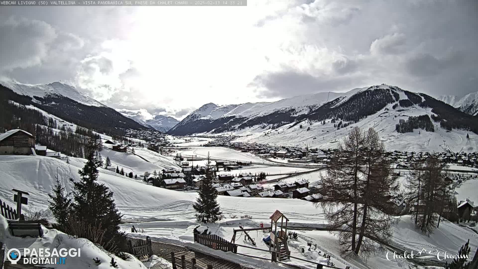 A snow-covered mountain village nestled in a valley under a partly cloudy sky.