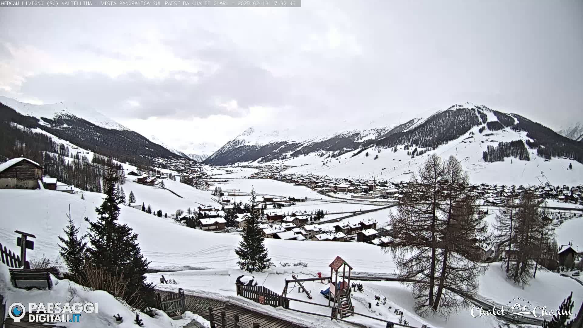 A snow-covered village nestled in a valley between snow-capped mountains under an overcast sky.