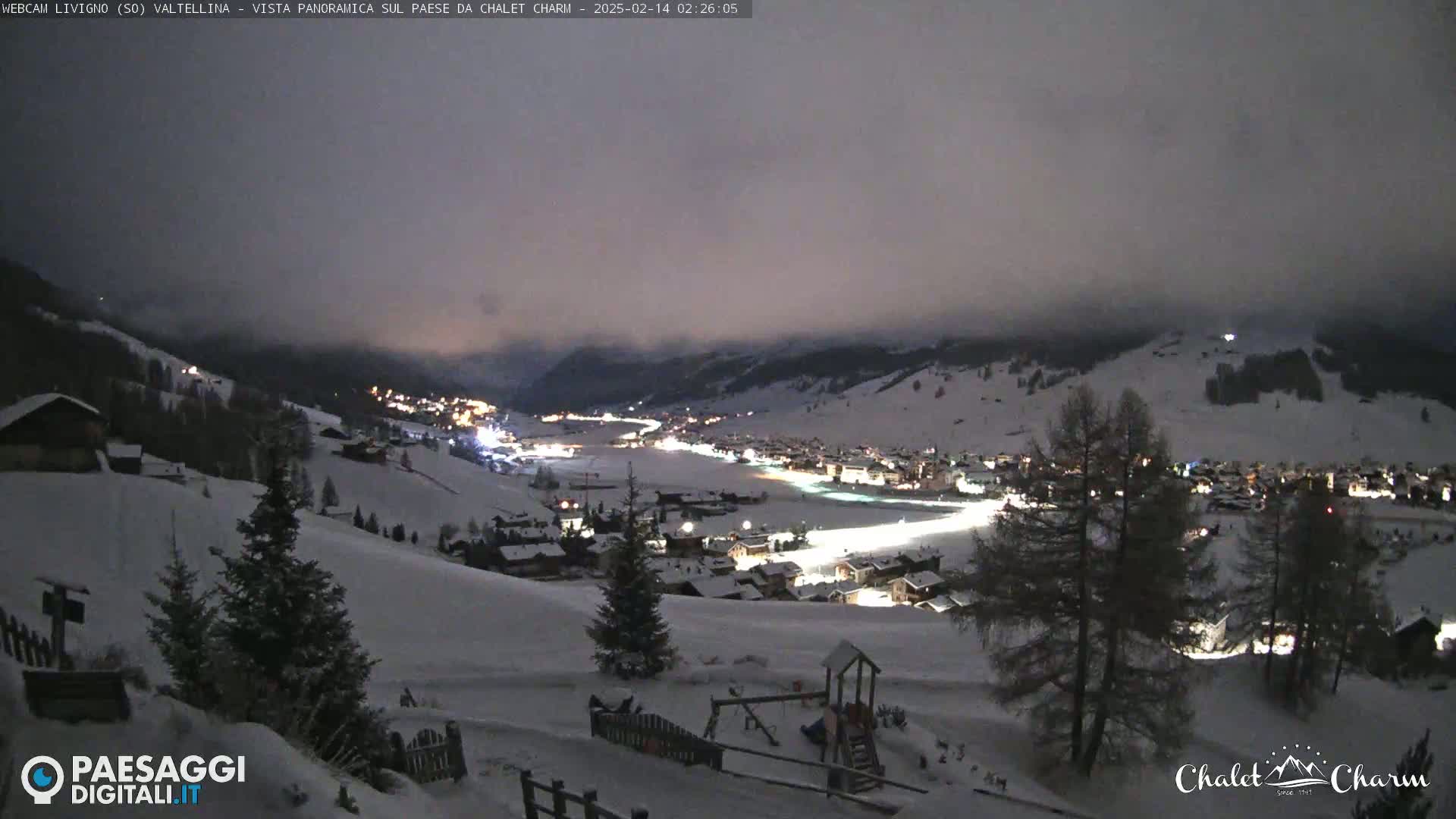 A snow-covered mountain village is illuminated at night under a cloudy sky.