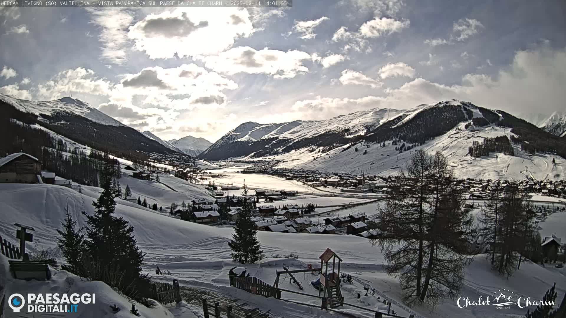 A snow-covered mountain village nestled in a valley under a partly cloudy sky.
