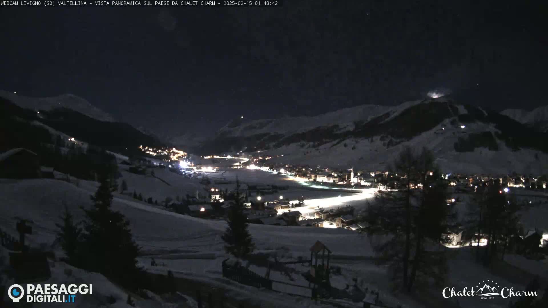 A nighttime, panoramic view of a snow-covered village nestled in a valley between mountains under a clear, dark sky.