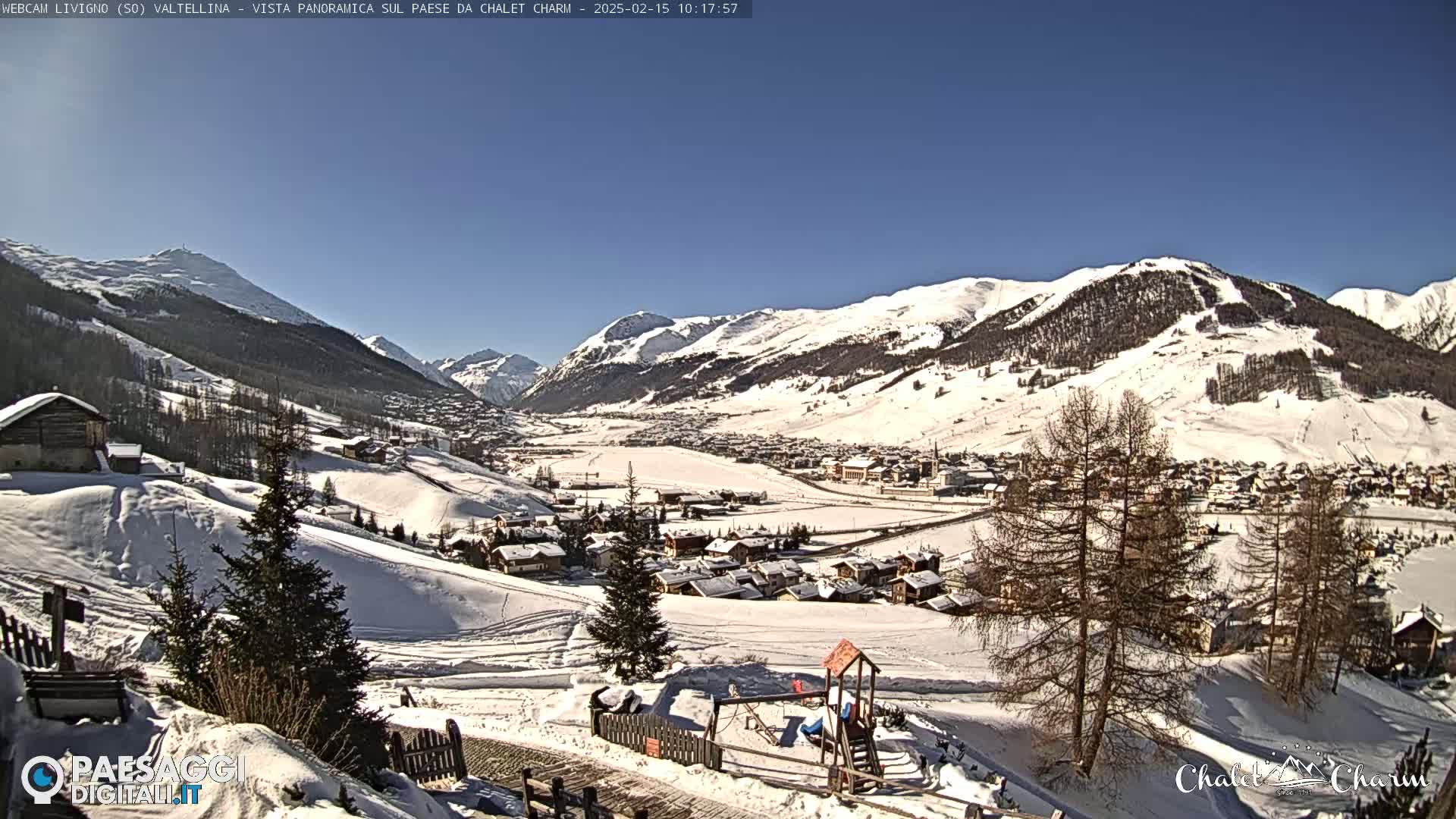 A snow-covered village nestled in a valley between snow-capped mountains on a sunny day.