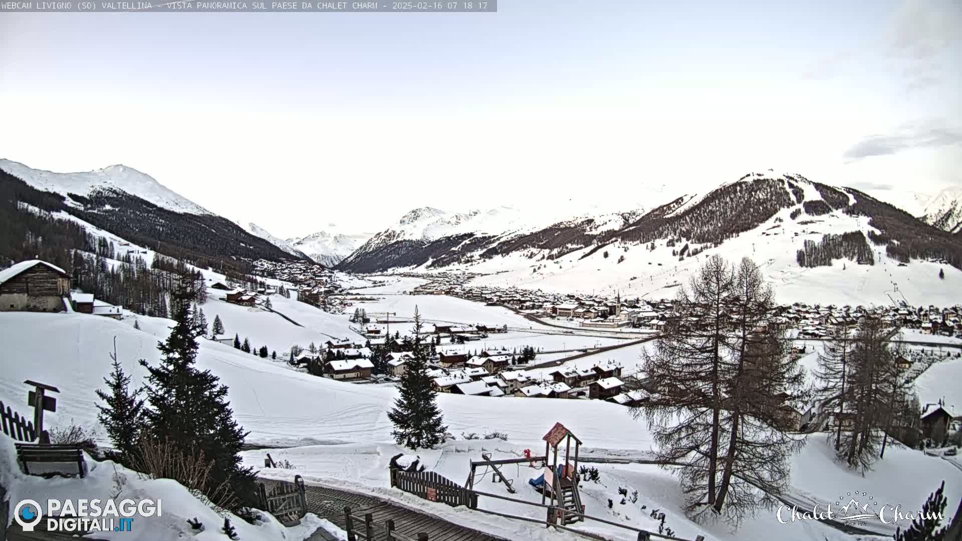 A snow-covered village nestled in a valley between snow-capped mountains under a mostly clear sky.