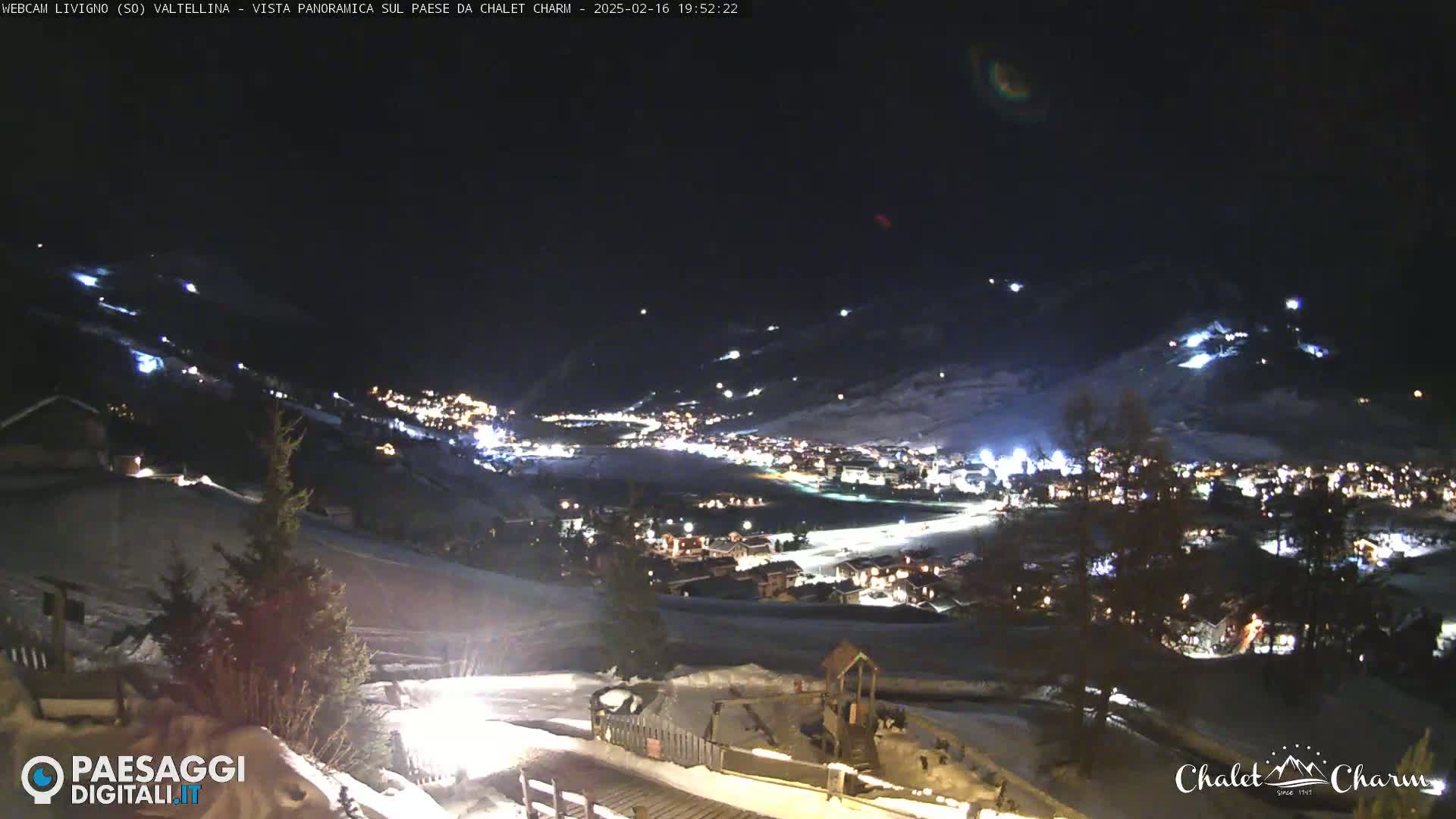 A nighttime, panoramic view of a snow-covered town illuminated by lights, seen from a higher vantage point.