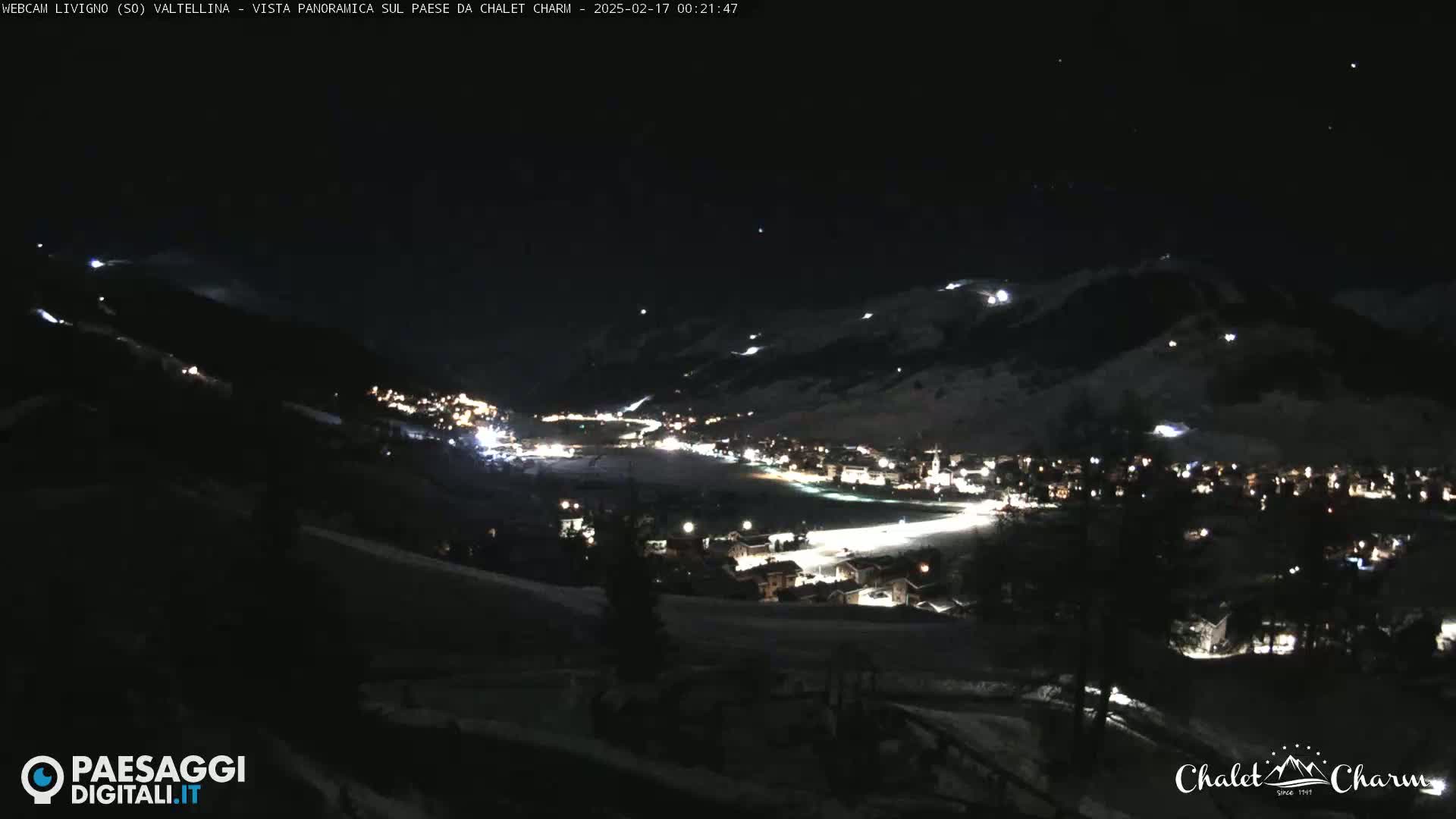 A nighttime, panoramic view of a snow-covered village nestled in a valley under a clear, starry sky.