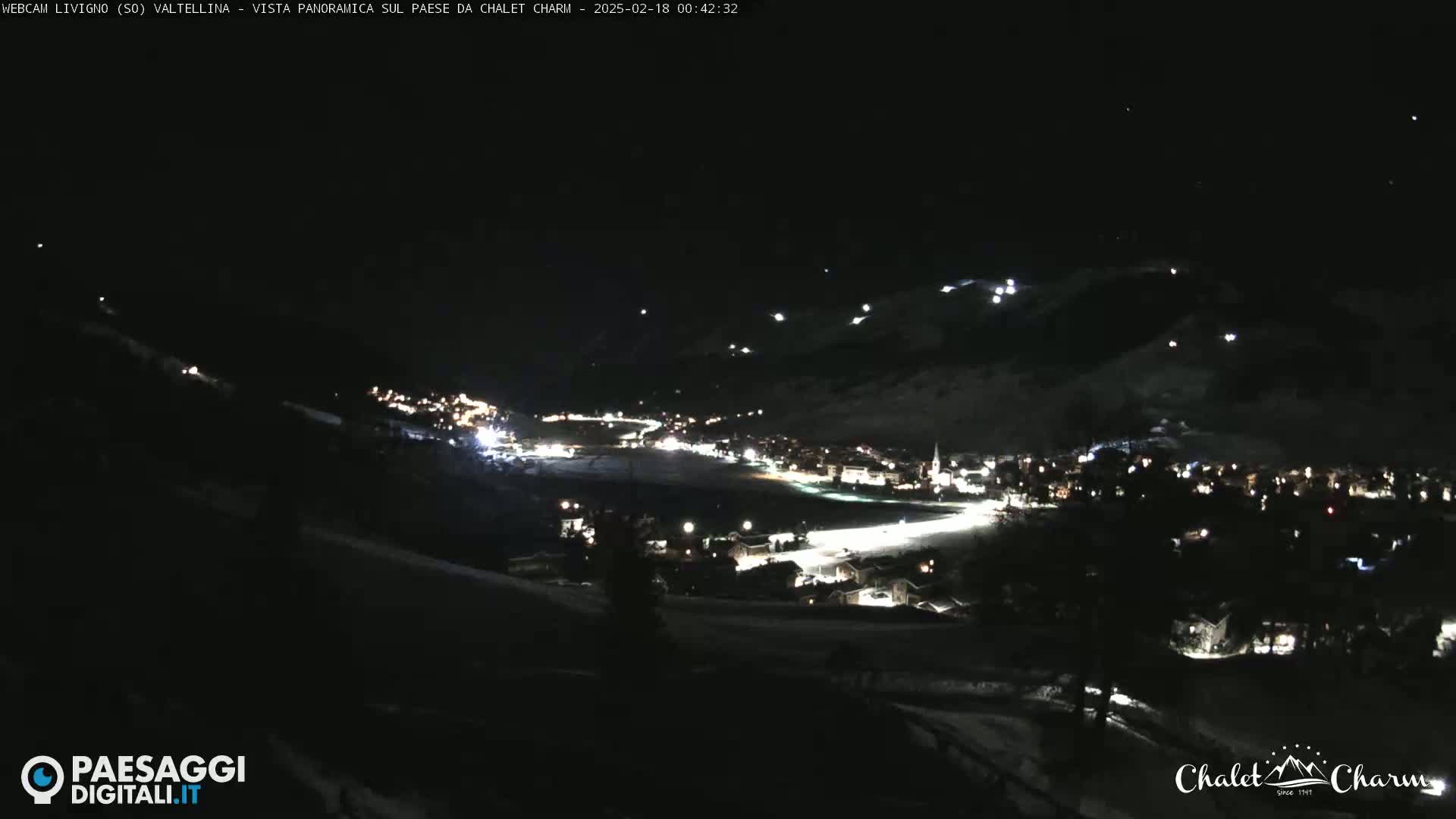 A nighttime, snow-covered mountain village is illuminated by scattered lights under a dark sky.