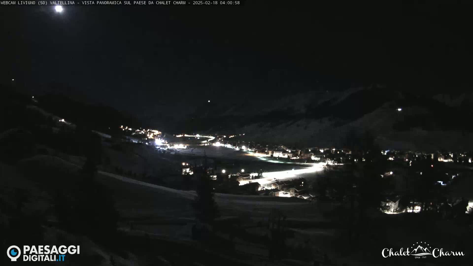 A nighttime, panoramic view of a snow-covered village illuminated by scattered lights under a dark, clear sky.