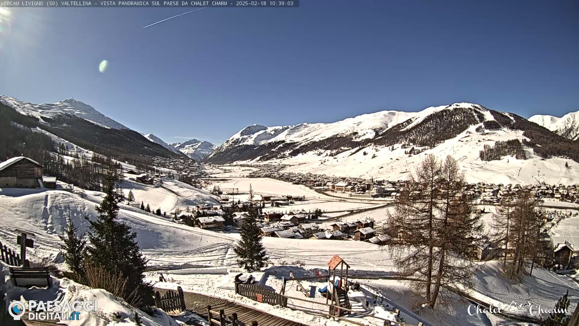 A snow-covered mountain valley town is viewed from a hillside on a sunny day.
