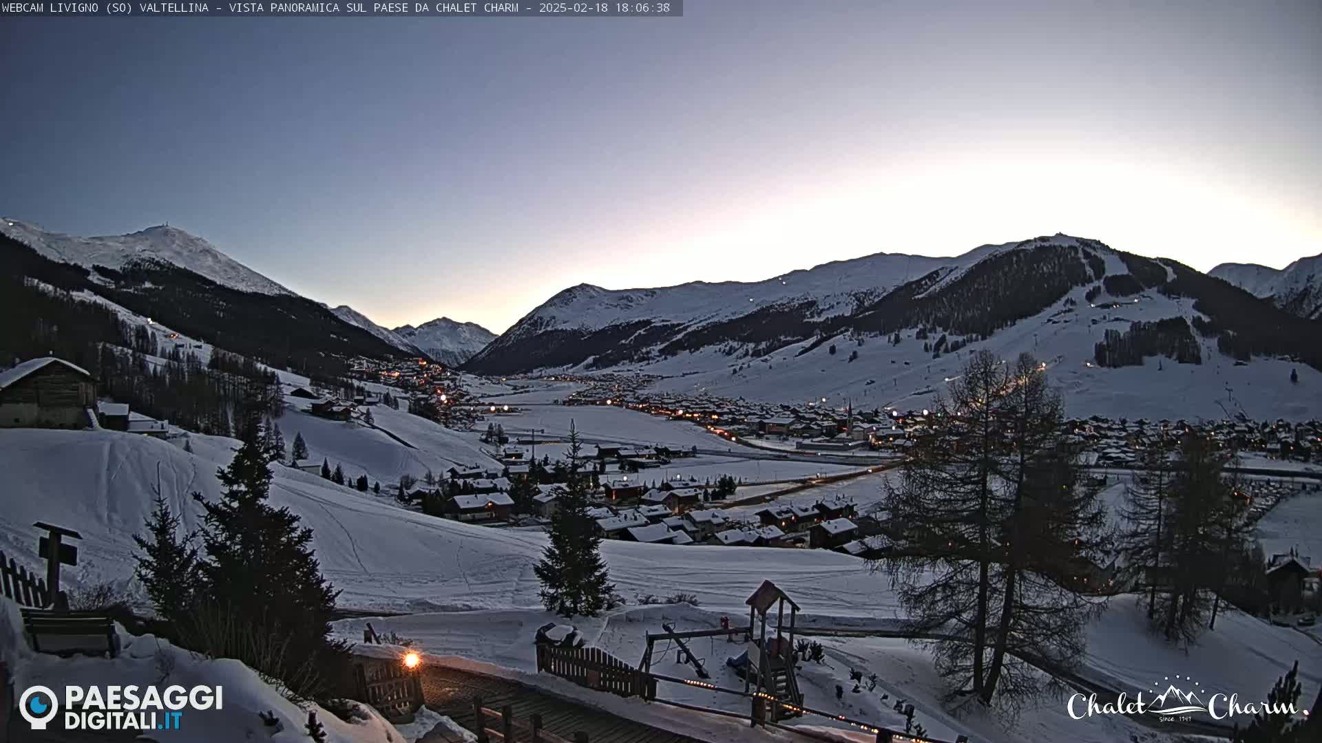 A snow-covered mountain village at twilight, with lights illuminating the houses and surrounding slopes.