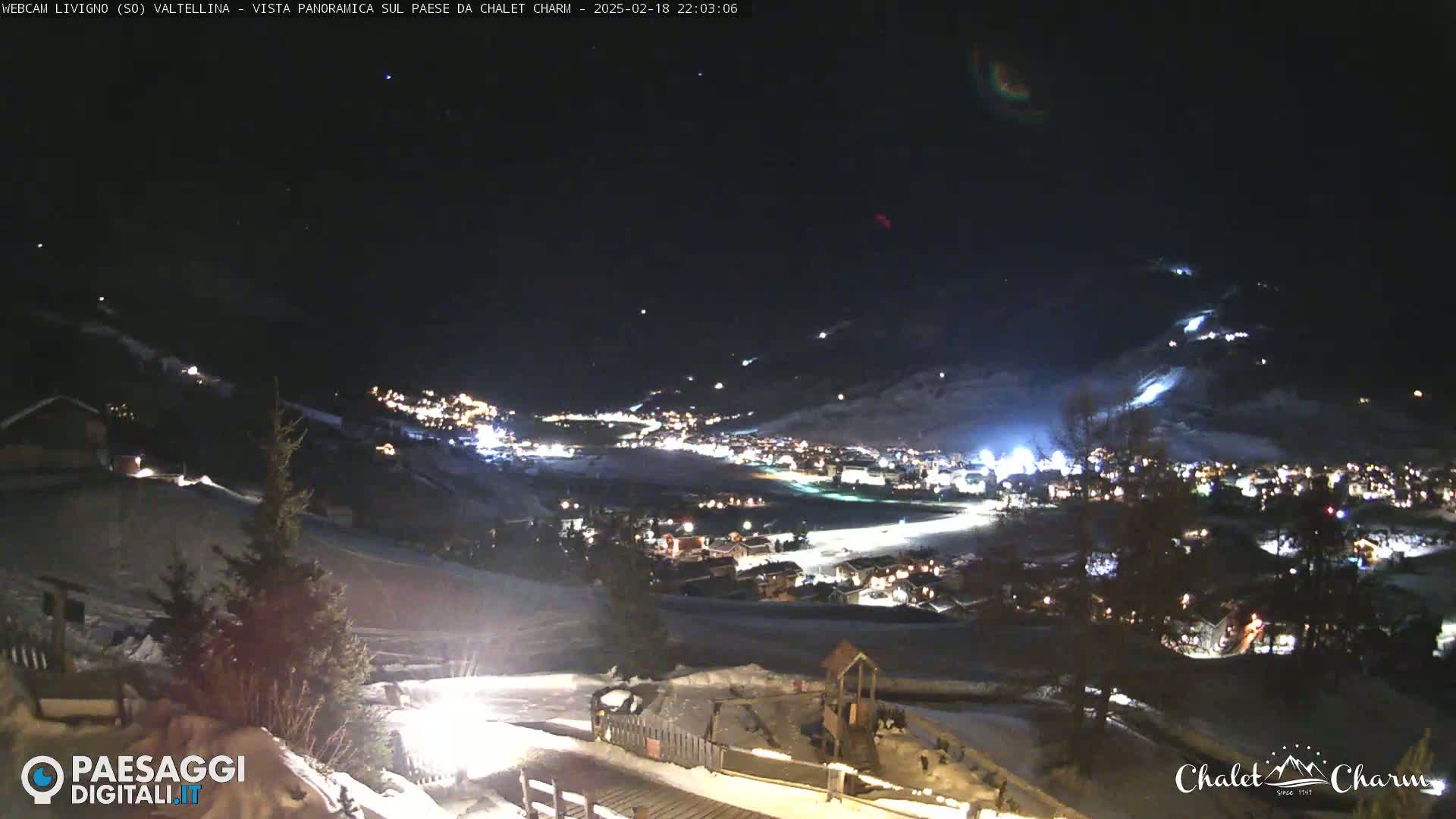 A nighttime, panoramic view of a snow-covered town illuminated by lights, with a clear sky above.