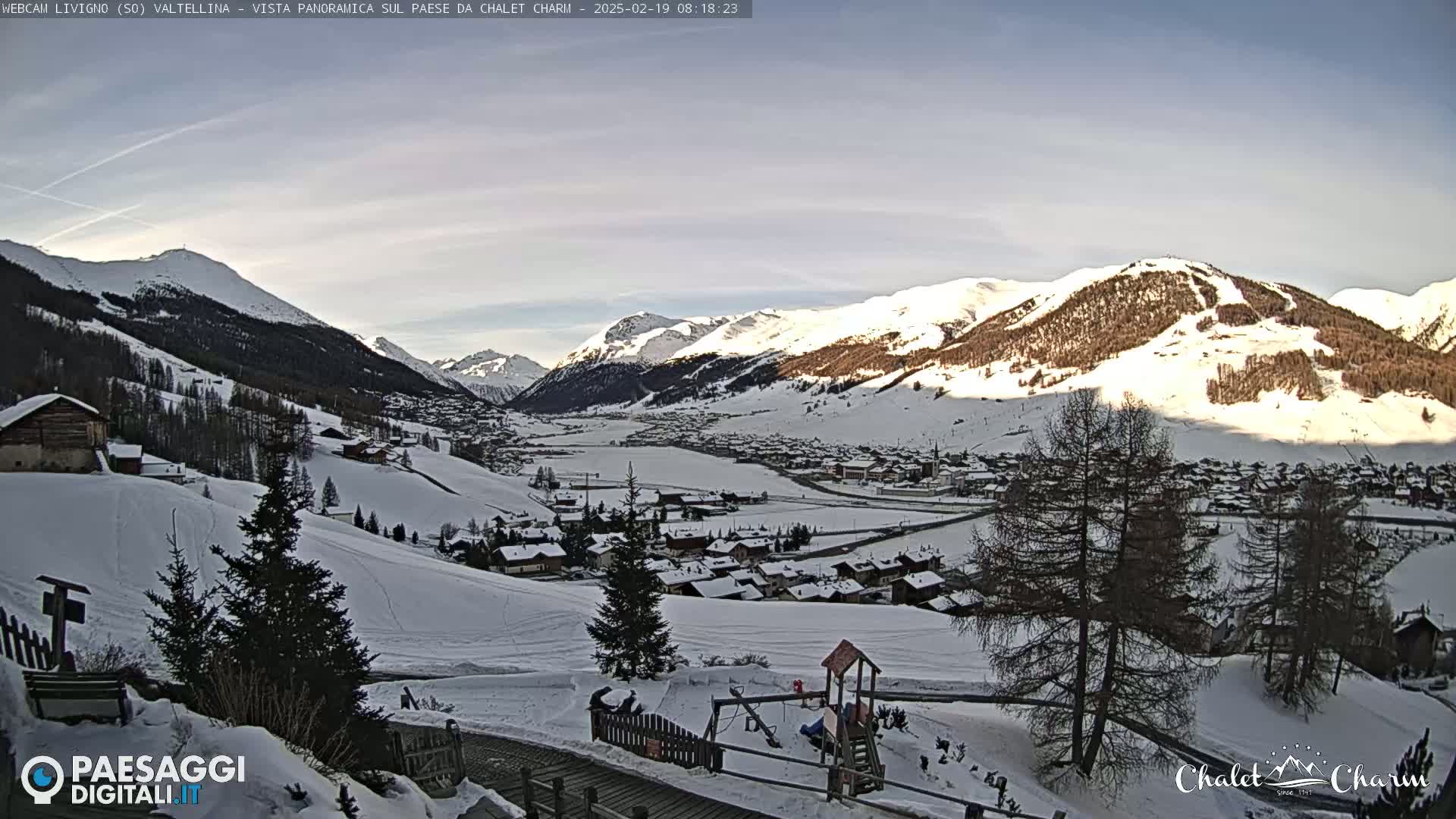 A snow-covered mountain village nestled in a valley between snow-capped mountains under a mostly clear sky.