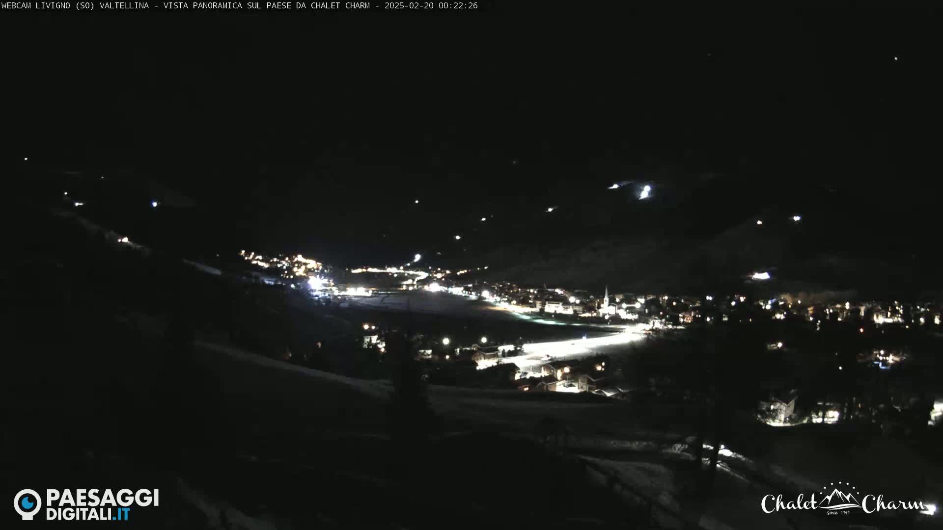 A nighttime panoramic view of a snow-covered town illuminated by scattered lights under a clear, dark sky.