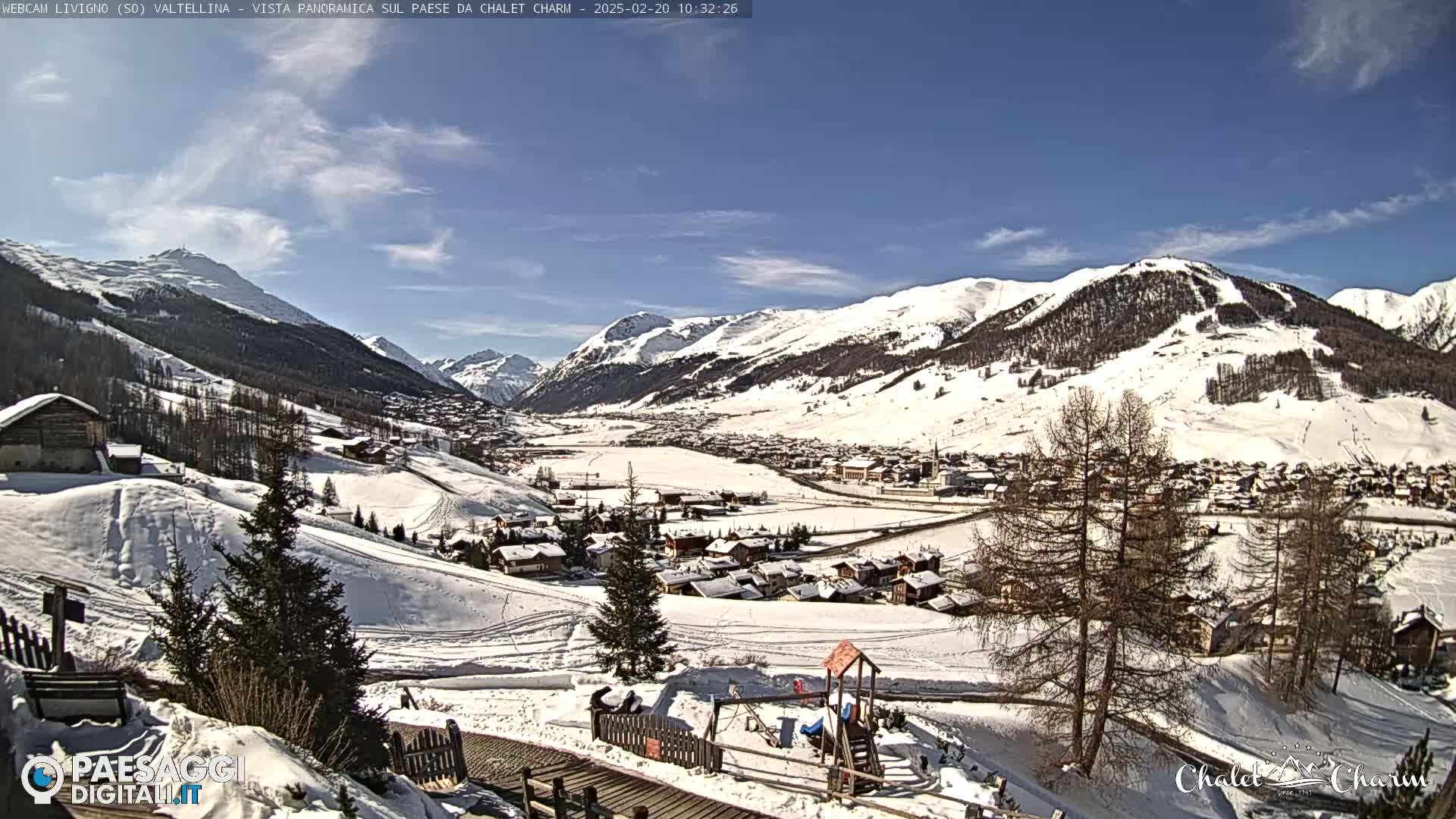 A snow-covered village nestled in a valley between snow-capped mountains under a mostly clear blue sky.
