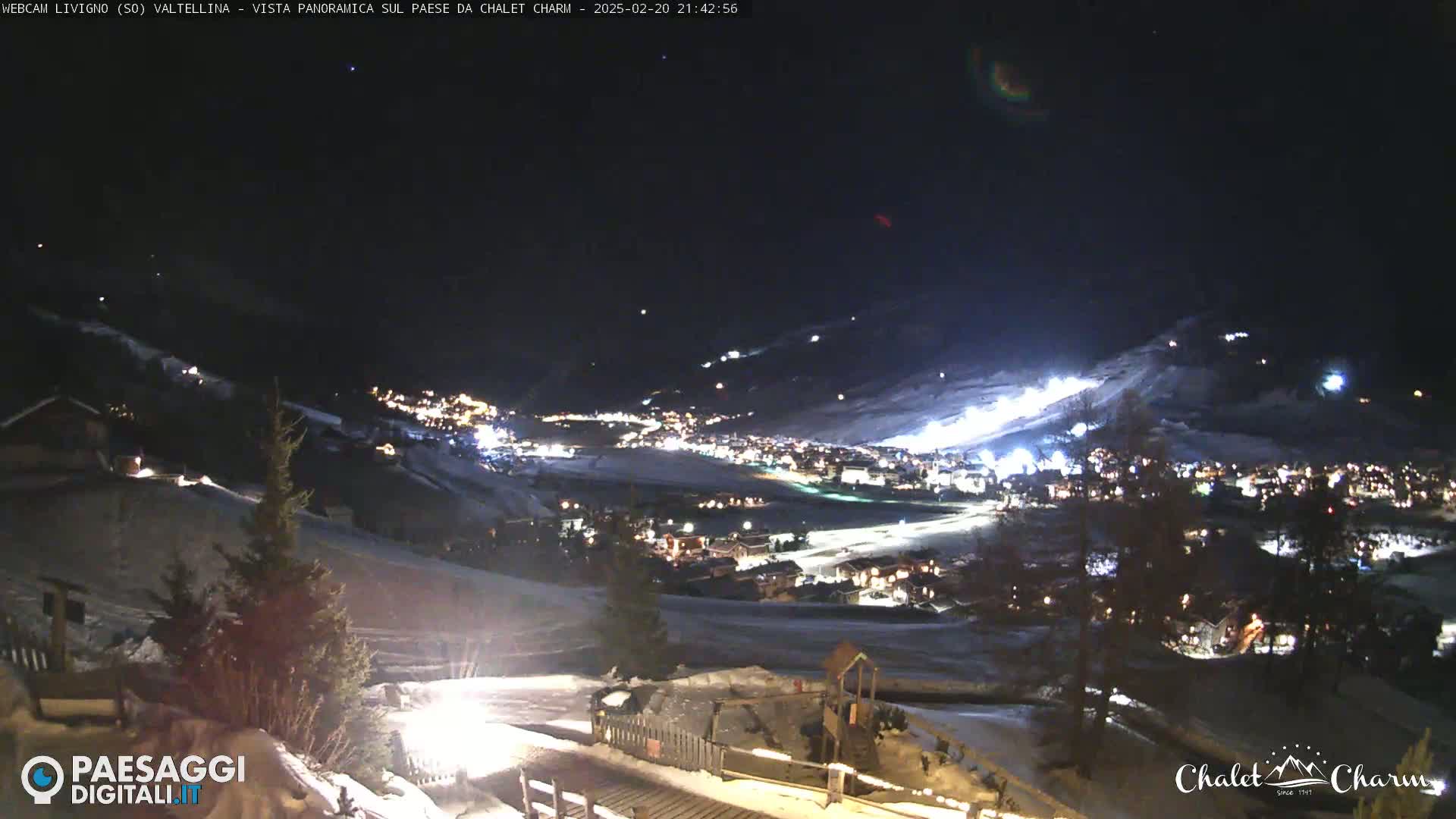A nighttime, panoramic view of a snow-covered town illuminated by lights, nestled in a valley under a dark, clear sky.