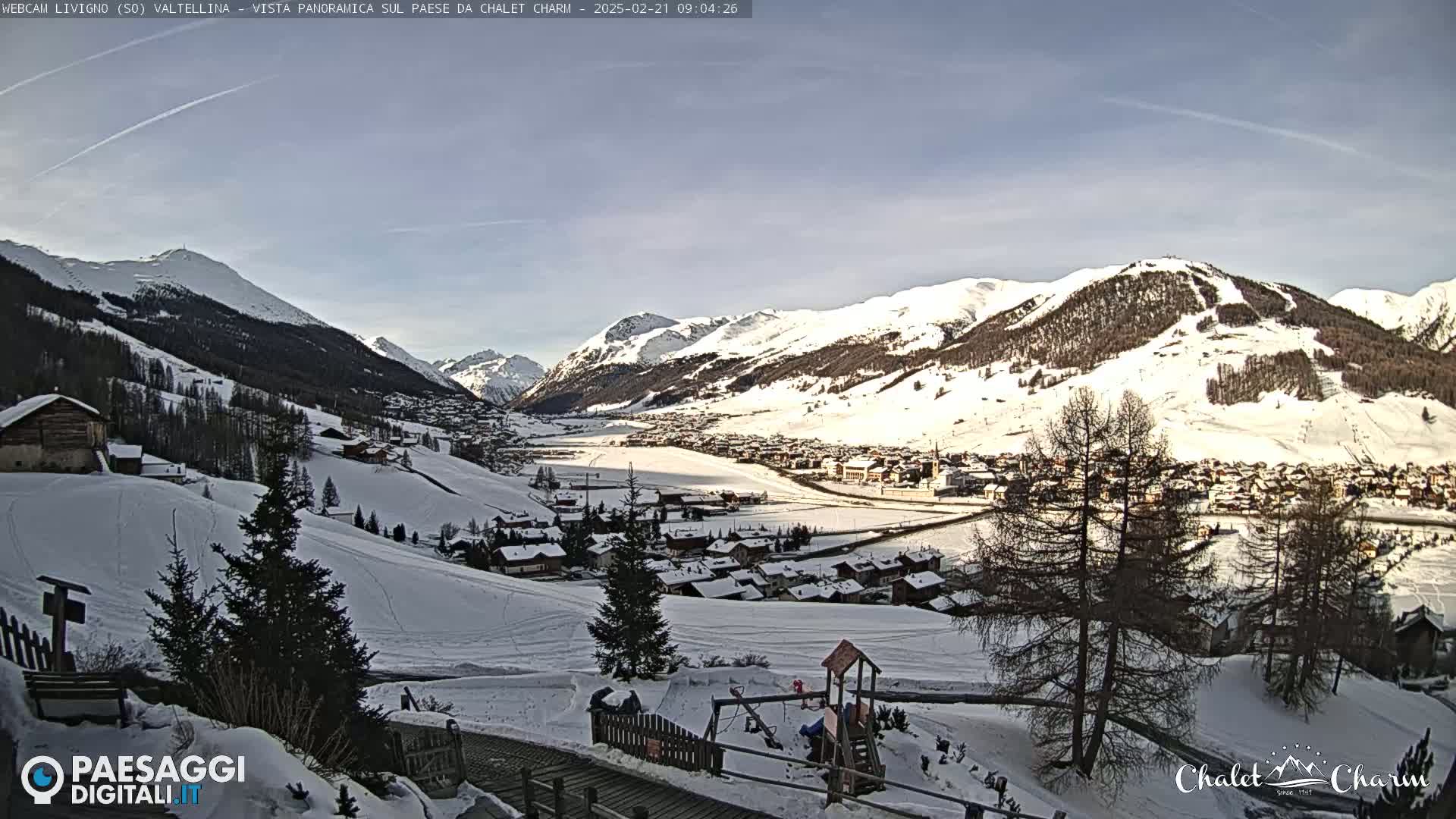 A snow-covered valley town nestled among snow-capped mountains under a mostly clear sky.