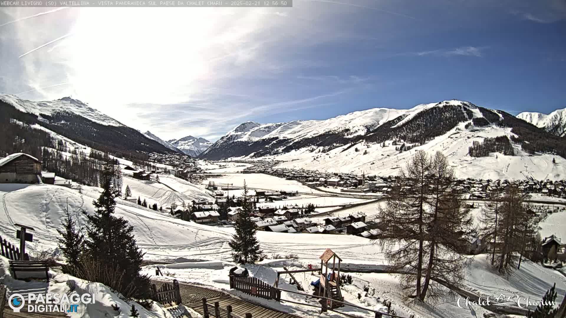 A snow-covered village nestled in a valley between snow-capped mountains on a sunny day.