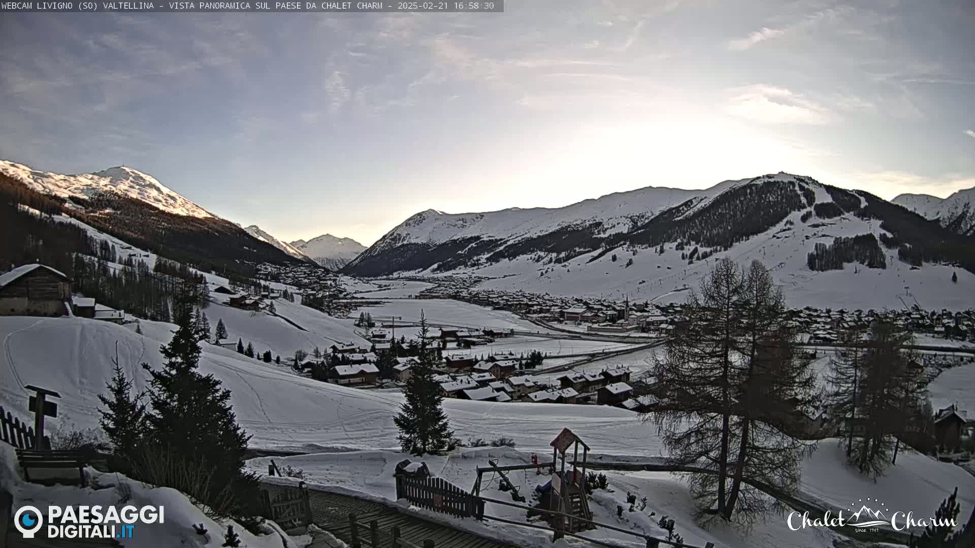 A snow-covered village nestled in a valley between snow-capped mountains, under a mostly clear twilight sky.