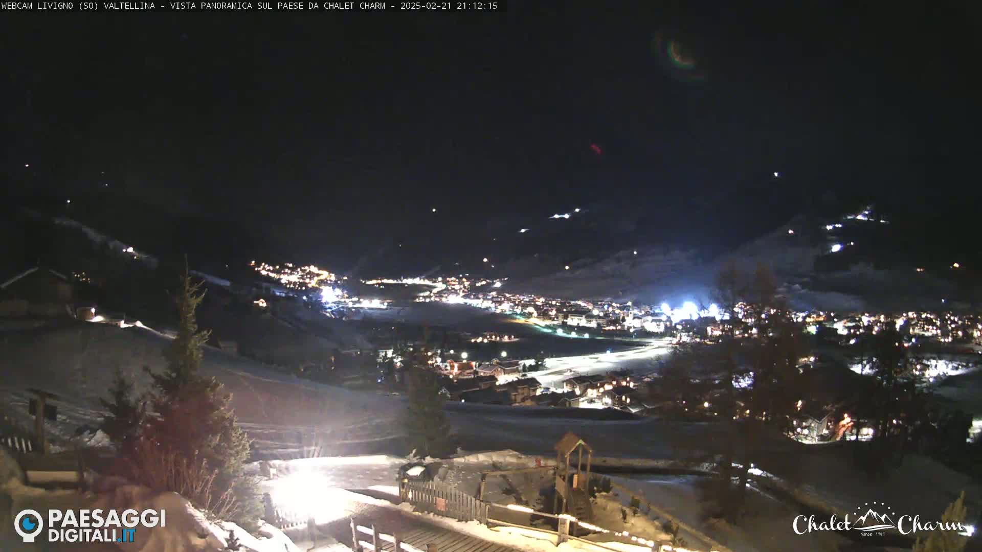 A nighttime, panoramic view of a snow-covered village illuminated by lights, with a clear sky.