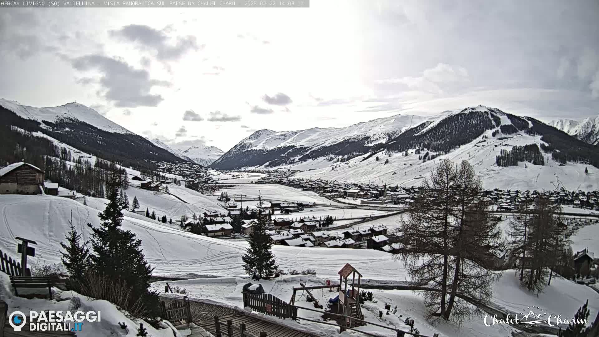 A snow-covered valley town nestled among snow-capped mountains under a cloudy sky.