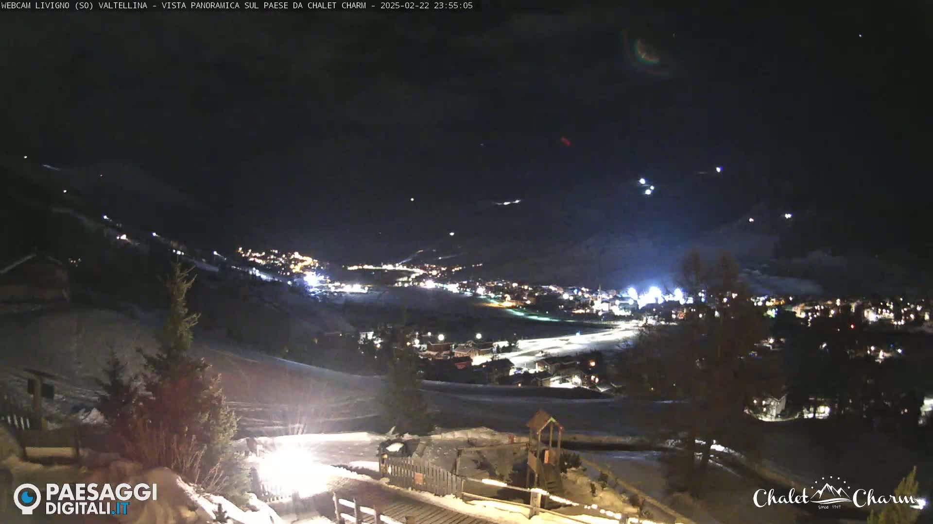 A nighttime, panoramic view of a snow-covered town illuminated by lights, under a dark, clear sky.