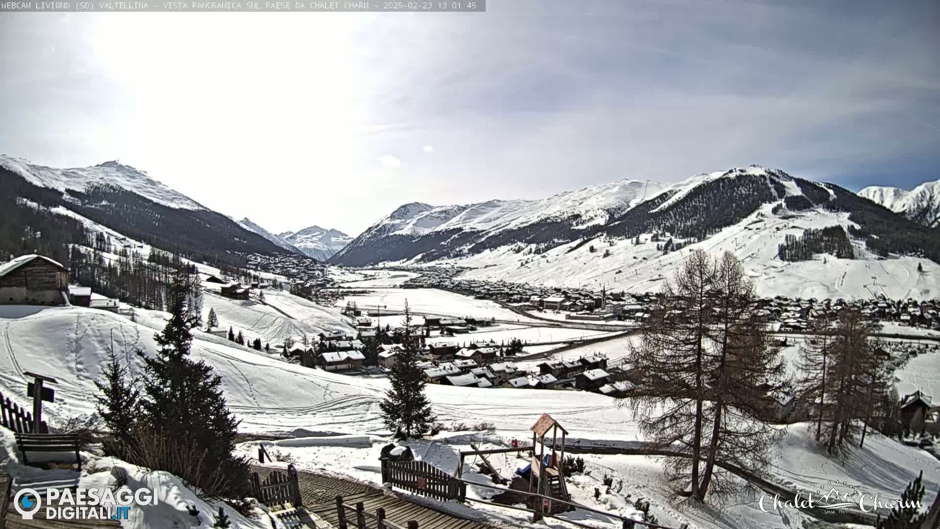 A snow-covered village nestled in a valley between snow-capped mountains under a mostly clear sky.