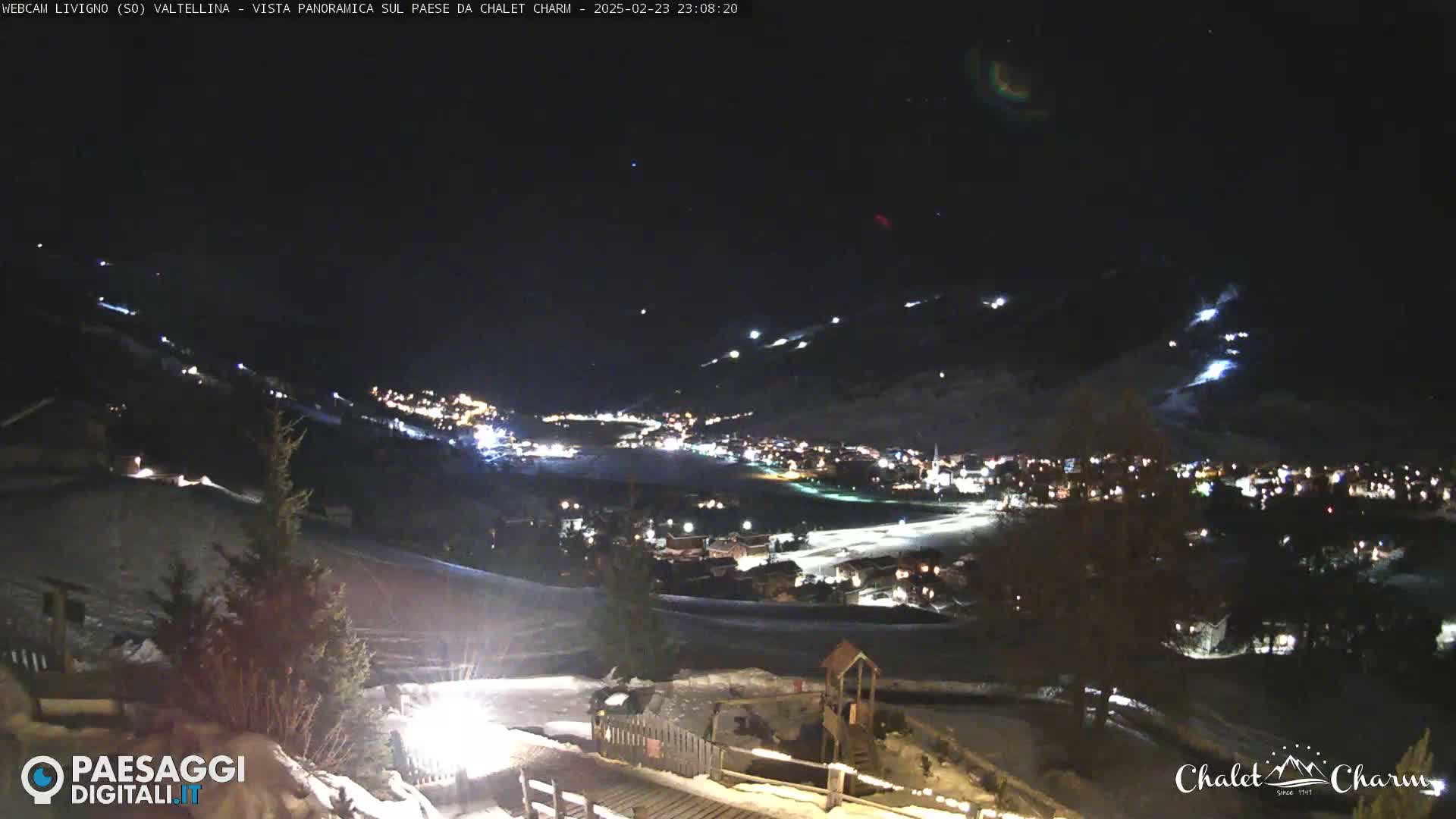 A nighttime panoramic view of a snow-covered town nestled in a valley, illuminated by scattered lights under a clear, dark sky.