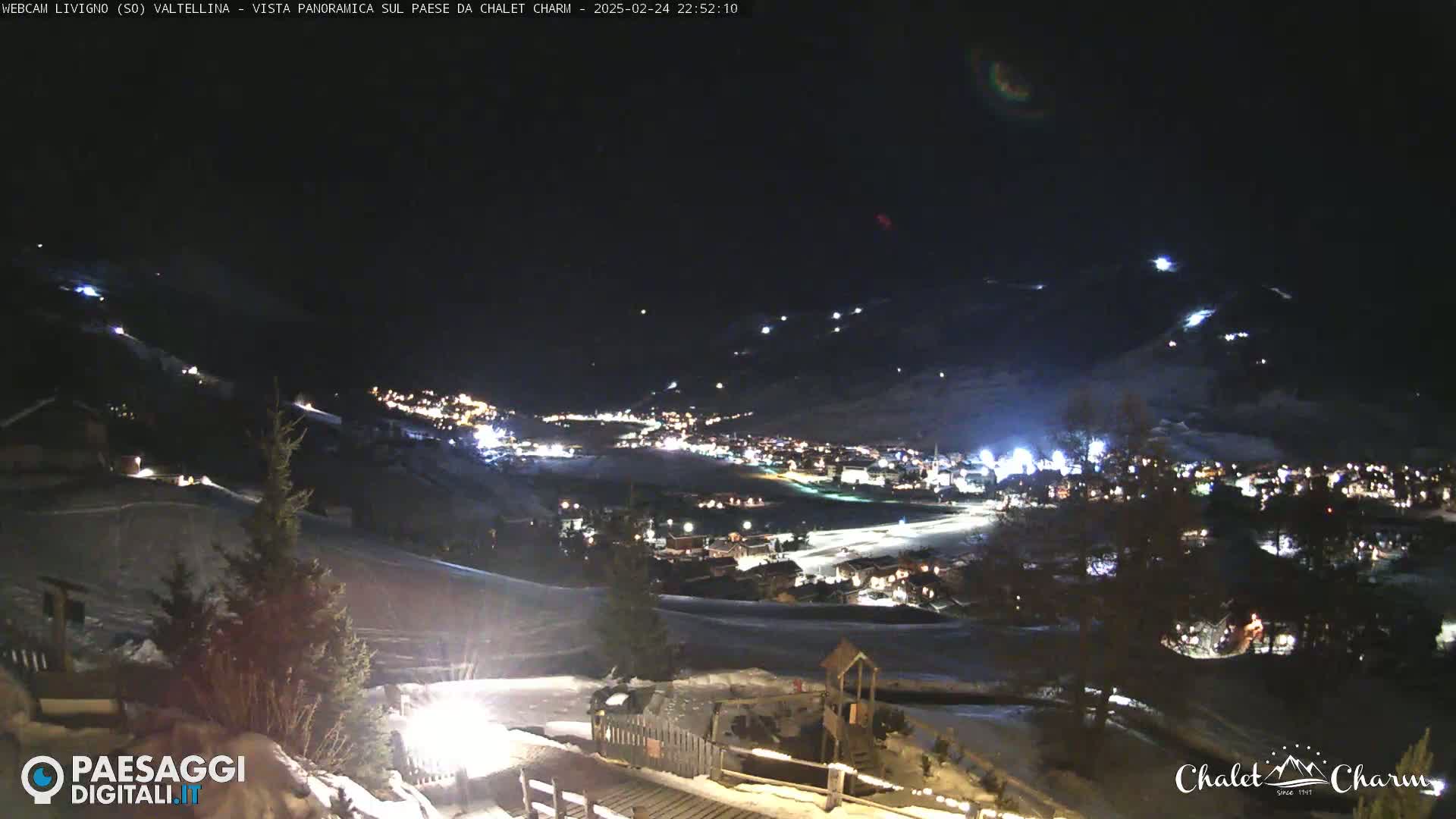 A nighttime, panoramic view of a snow-covered town illuminated by lights, with a clear, dark sky above.