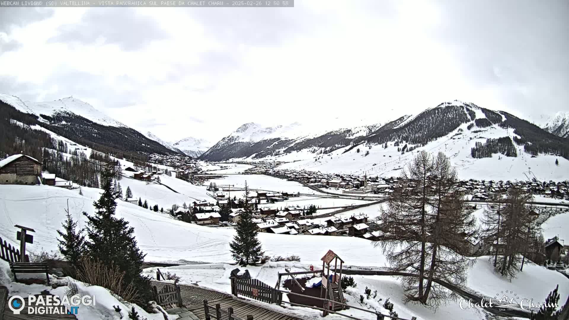 A snow-covered village nestled in a valley between snow-capped mountains under an overcast sky.