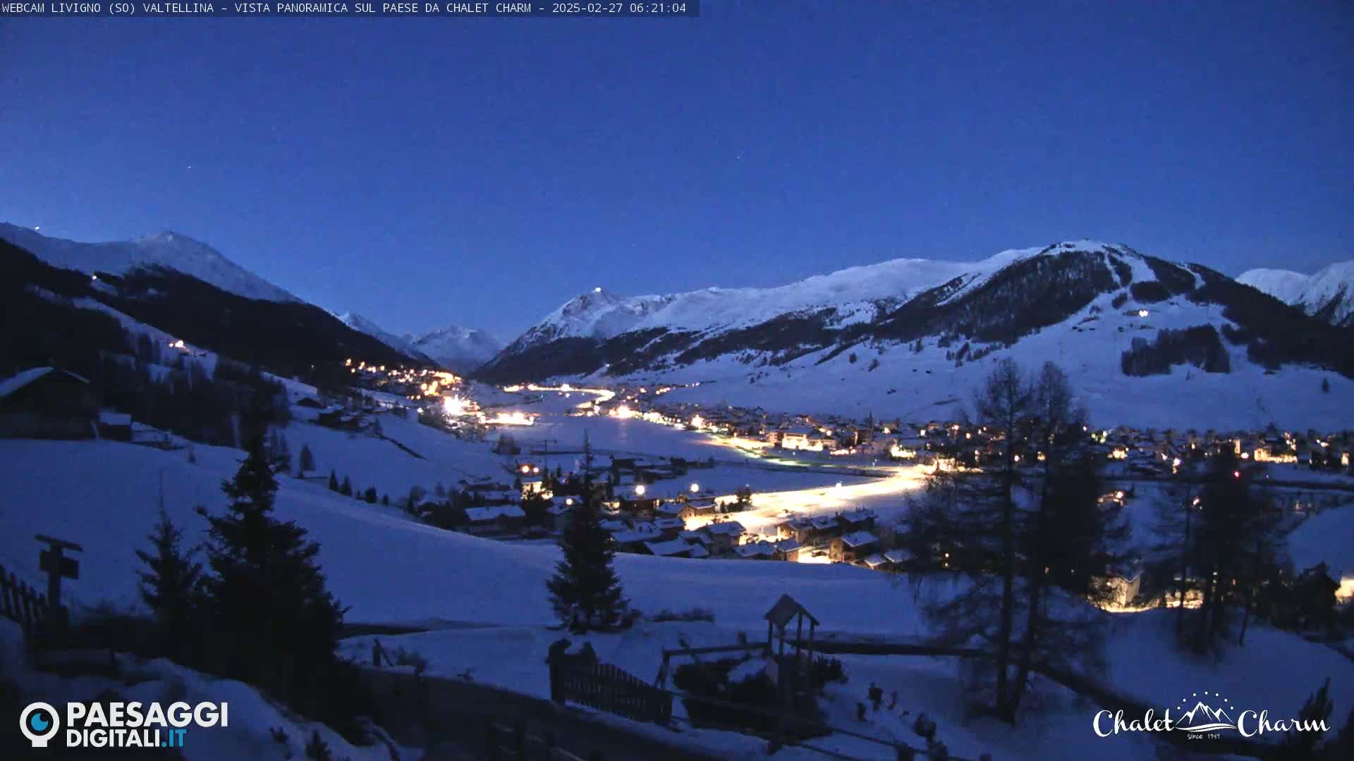 A snow-covered mountain village is illuminated at night under a twilight sky.