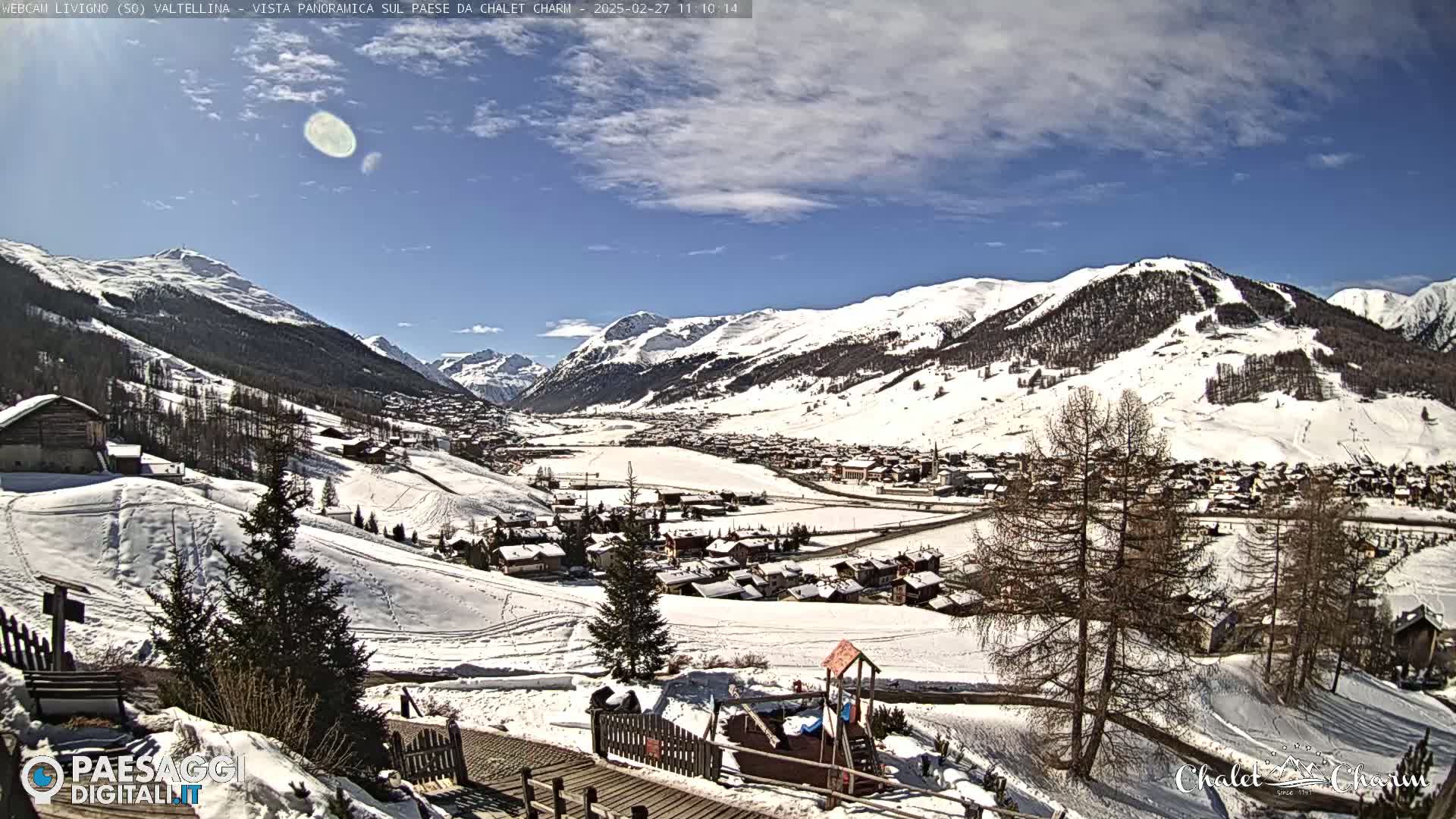 A snow-covered mountain village is viewed from a hillside on a partly sunny day.